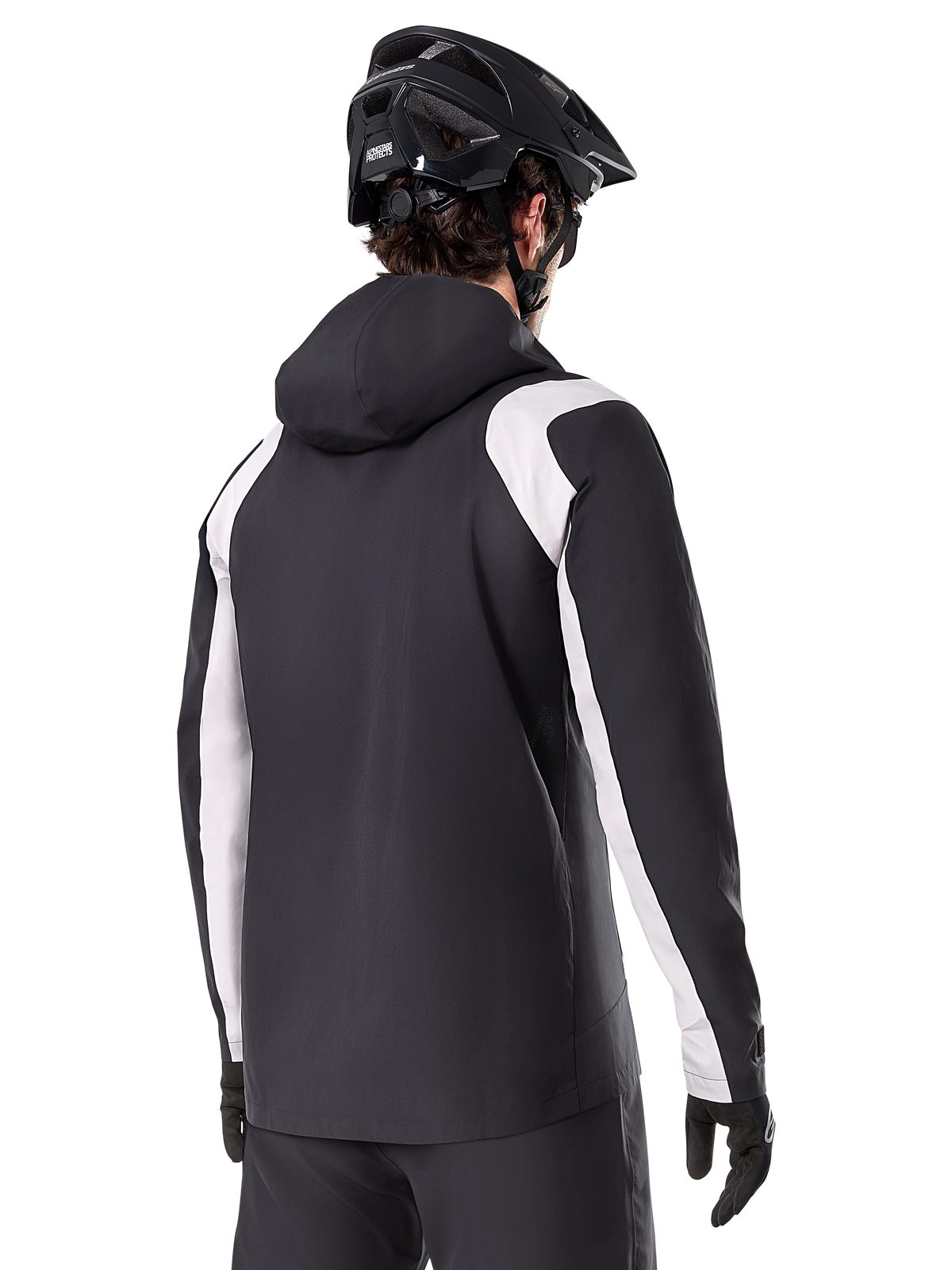 Alpinestars Giacca Antipioggia A-Dura, giacca antipioggia da mountain bike, nera con pannelli bianchi sulle maniche, vista posteriore del ciclista con casco da MTB nero e guanti, costruzione tecnica impermeabile a 2,5 strati, abbigliamento da mountain bike