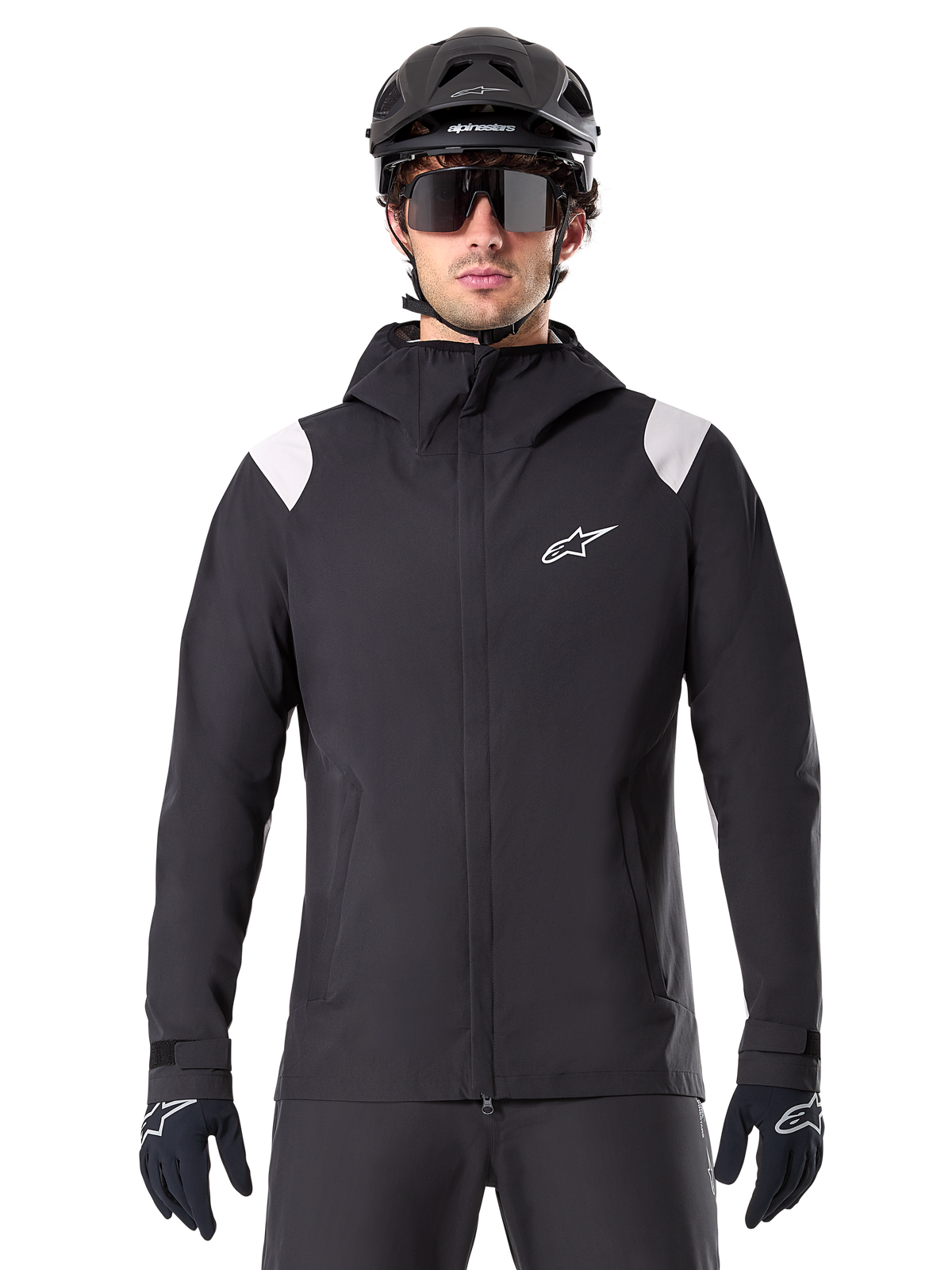 Alpinestars A-Dura Rain Jacket, giacca antipioggia MTB, nero con pannelli bianchi sulle spalle, indossata con casco MTB nero, occhiali da sole e guanti, design impermeabile con cappuccio e cerniera frontale, abbigliamento sportivo outdoor per il ciclismo