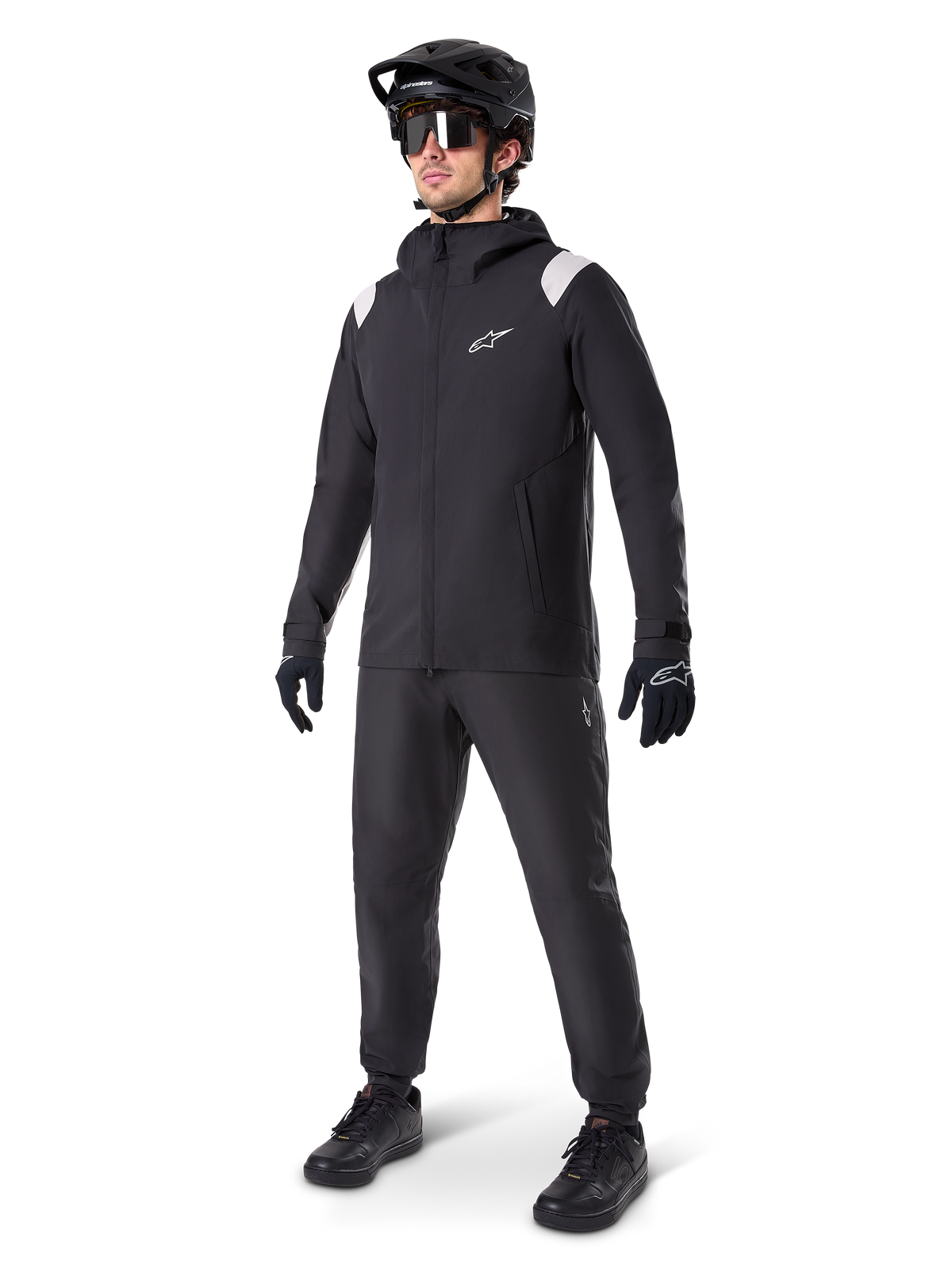 Alpinestars A-Dura Rain Jacket, giacca antipioggia da mountain bike nera, con accenti bianchi sulle spalle, indossata da un ciclista con casco da MTB, occhiali da sole, guanti e pantaloni neri coordinati, abbigliamento tecnico da ciclismo per ogni condizione meteo