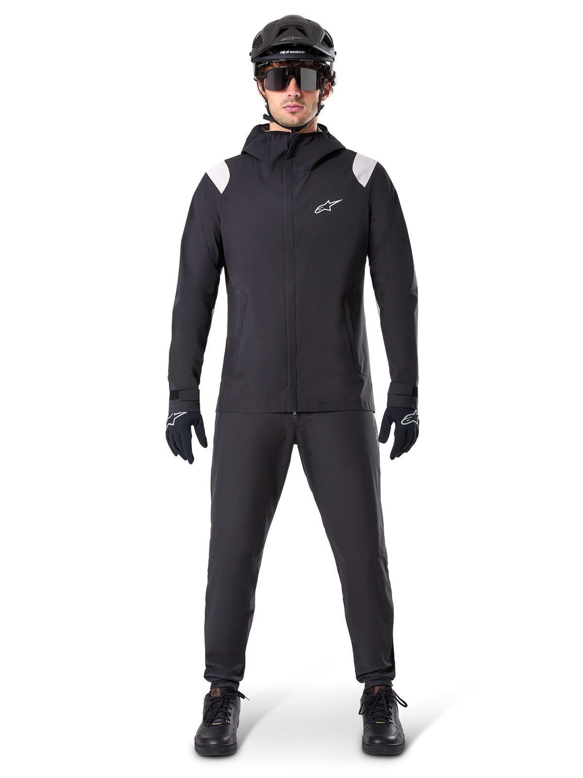 Giacca Antipioggia Alpinestars A-Dura, giacca antipioggia da mountain bike, nera con accenti bianchi sulle spalle e logo bianco sul petto, indossata con pantaloni neri, casco nero, occhiali da sole e guanti, abbigliamento coordinato da mountain bike per il maltempo