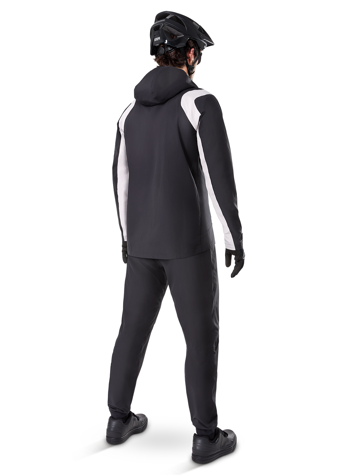 Alpinestars Giacca Antipioggia A-Dura, vista posteriore di un ciclista che indossa la giacca da MTB impermeabile bianca e nera, pantaloni da ciclismo neri coordinati, casco e guanti neri, equipaggiamento tecnico per mountain bike in condizioni di pioggia