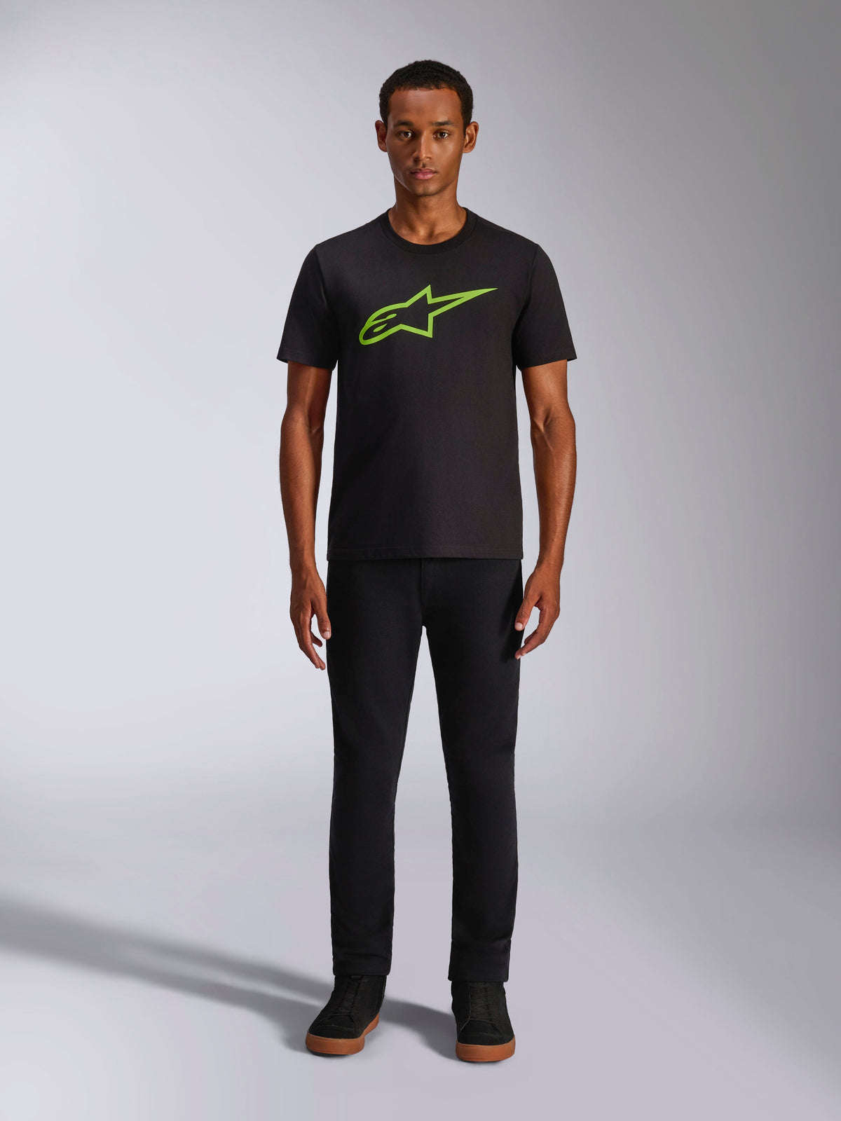 Alpinestars Ageless 2.0 CSF Tee, maglietta a maniche corte, nero con logo verde brillante, indossata da un modello con pantaloni neri, design casual ispirato al motorsport