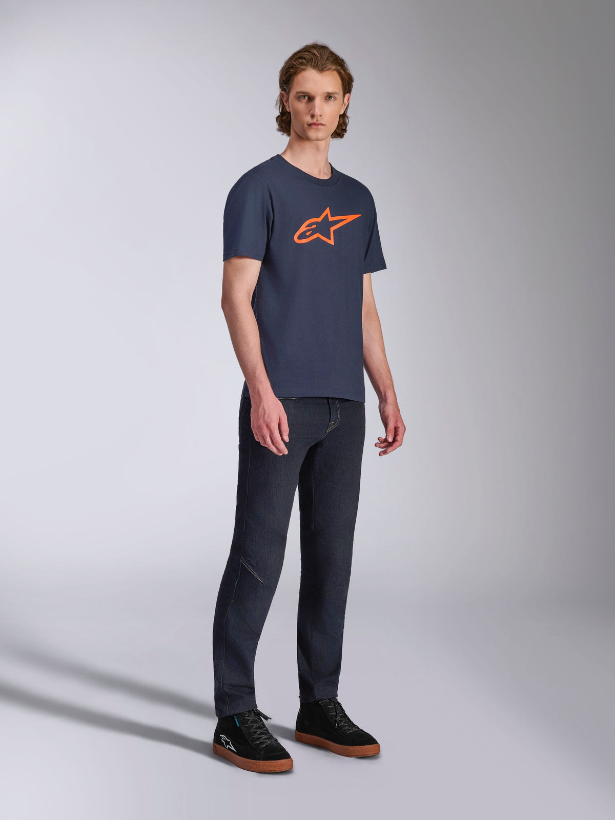 Alpinestars Ageless 2.0 CSF Tee, maglietta a maniche corte, blu navy con logo a stella arancione, indossata con jeans in denim scuro e sneakers nere, abbigliamento streetwear casual ispirato al motorsport