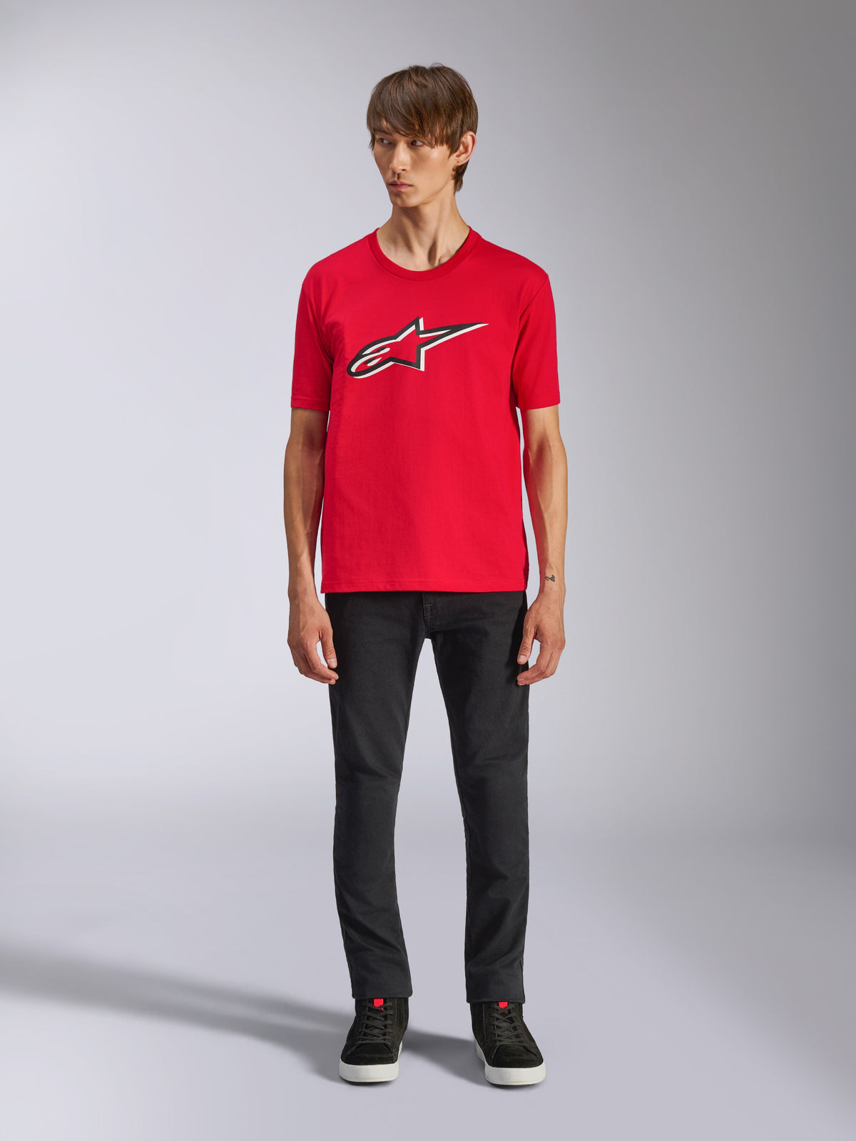 Alpinestars Ageless Shadow CSF Tee, t-shirt a maniche corte, rosso, logo Ageless frontale con contorni bianchi e neri, indossata da un modello con pantaloni neri e sneakers, casual motorsport streetwear
