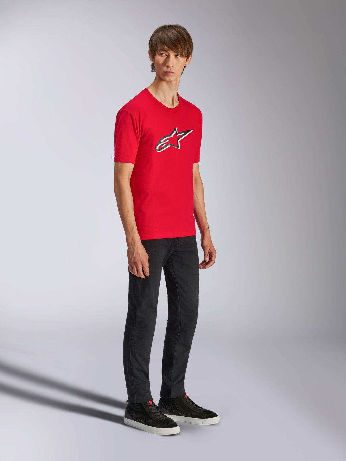 Alpinestars Ageless Shadow CSF Tee, t-shirt rossa a maniche corte, con un grande logo Ageless sul petto, indossata da un modello con pantaloni neri e sneakers, streetwear casual motorsport