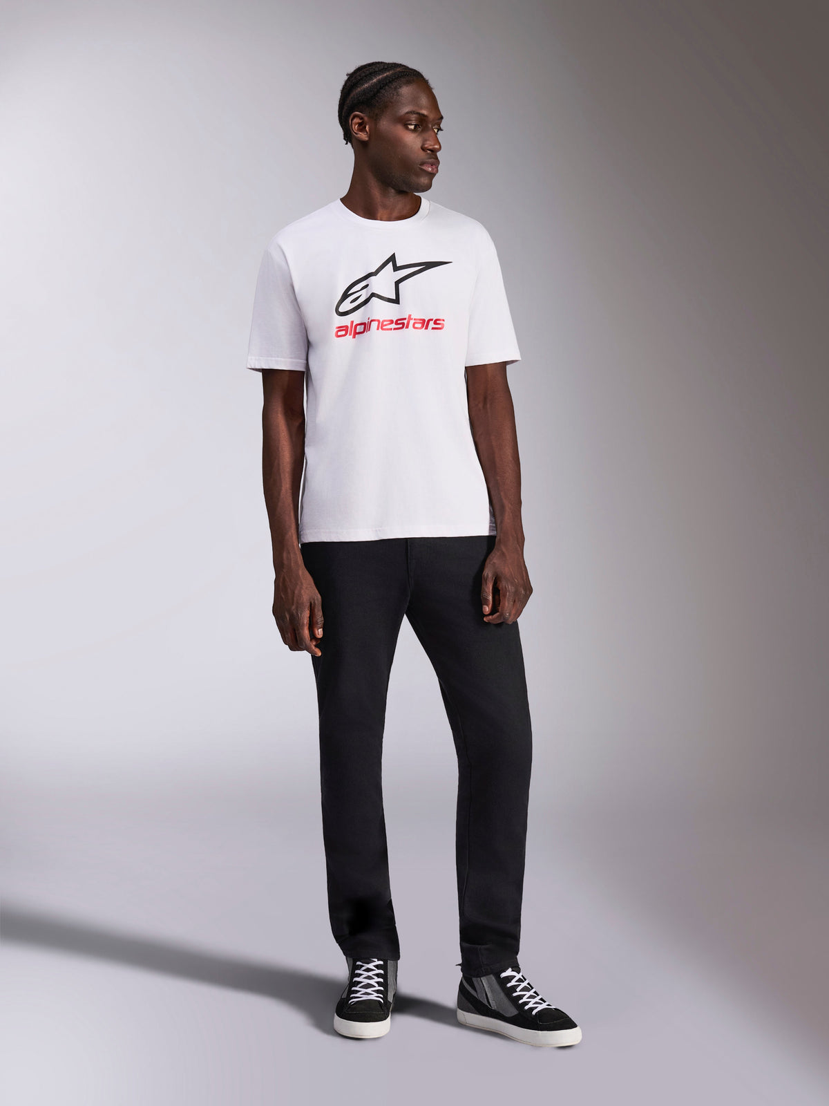 Alpinestars Always 2.0 CSF Tee, T-shirt a maniche corte, bianca, logo Astar nero e grafica wordmark Alpinestars rossa, indossata da un modello con pantaloni neri e sneakers alte, abbigliamento sportivo casual motorsport