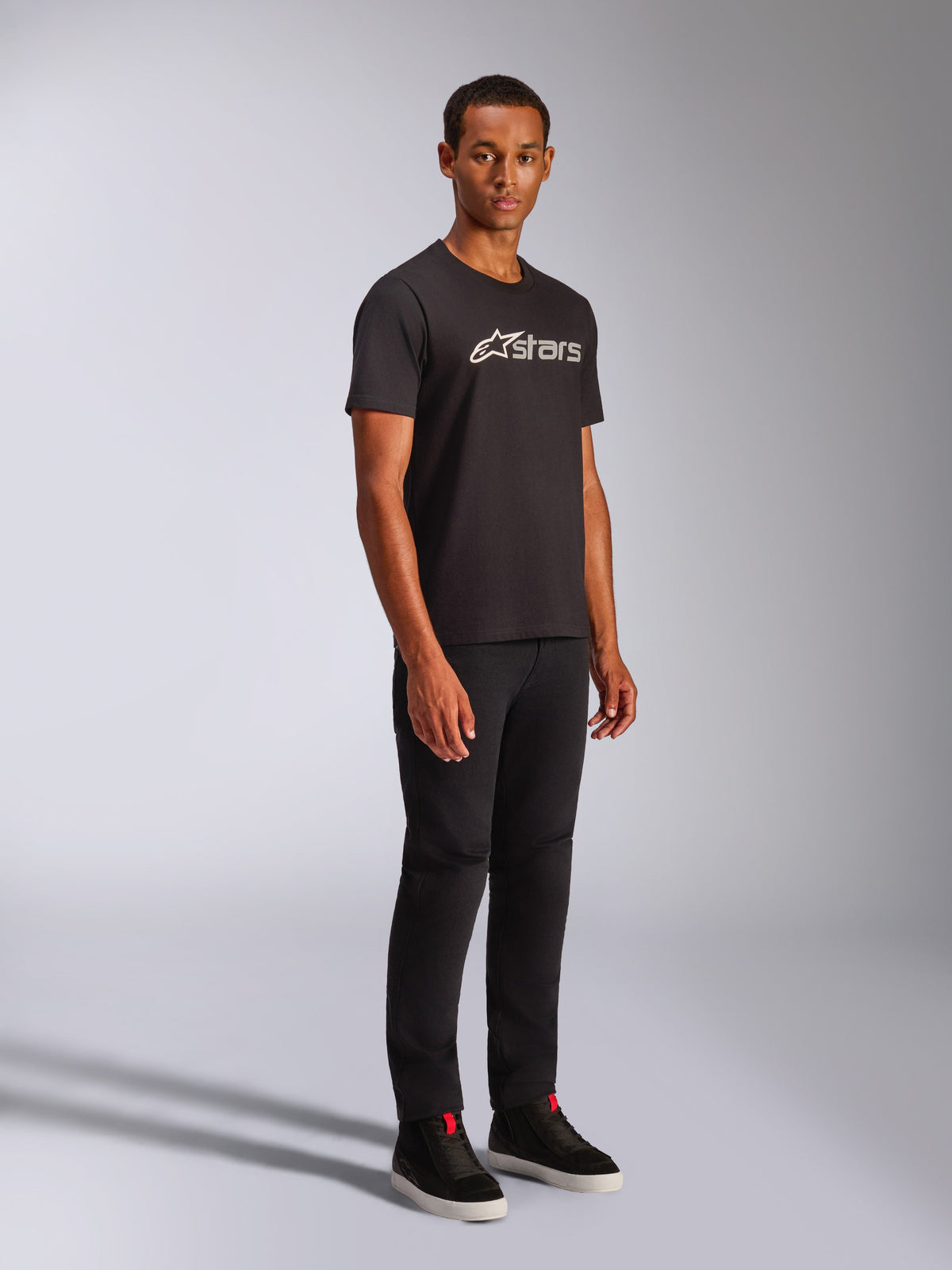 Alpinestars Blaze 2.0 CSF Tee, maglietta a maniche corte, nera con grafica logo bianca e grigia, indossata da un modello con pantaloni neri e sneakers alte, streetwear casual motorsport