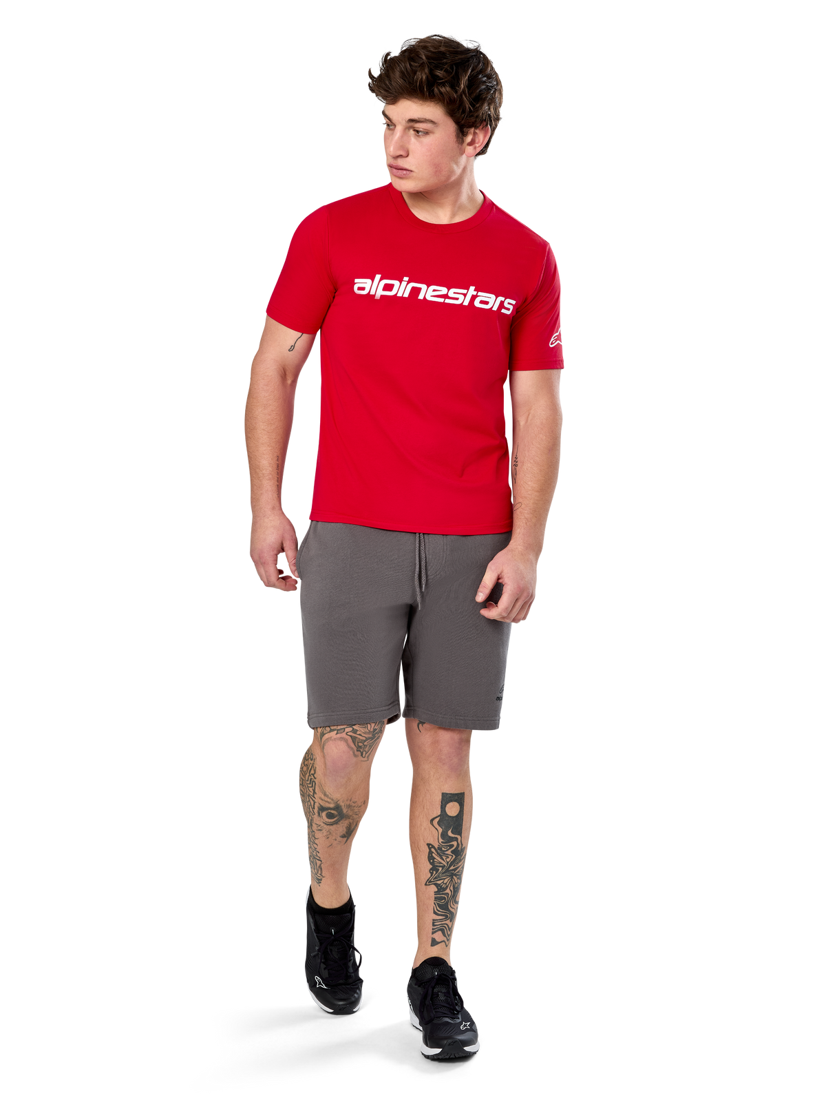 Alpinestars Linear Wordmark 2.0 CSF Tee, t-shirt a maniche corte, rossa con logo wordmark bianco sul petto, indossata da un modello con pantaloncini grigi e sneakers nere, streetwear casual ispirato al motorsport