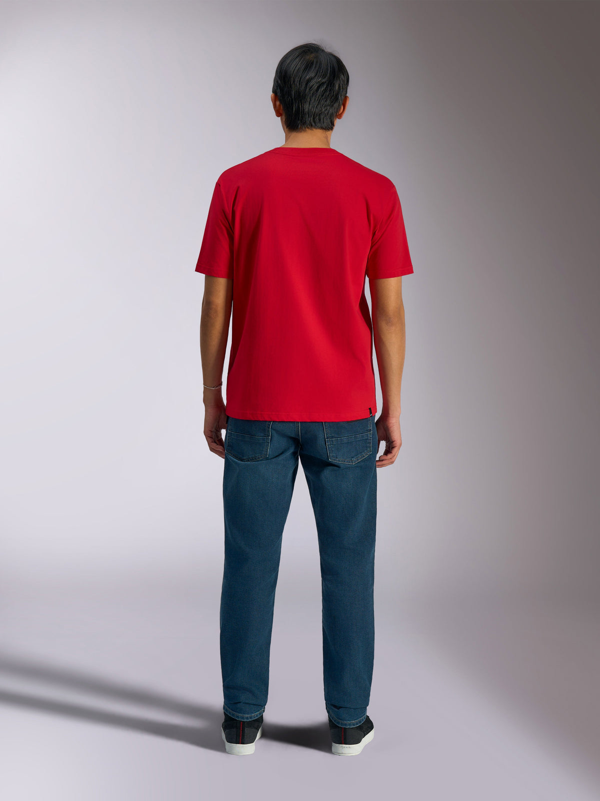 Alpinestars Ageless Shadow CSF Tee, vista posteriore della maglietta rossa a maniche corte, indossata con jeans in denim blu scuro e sneakers nere, abbigliamento casual motorsport streetwear