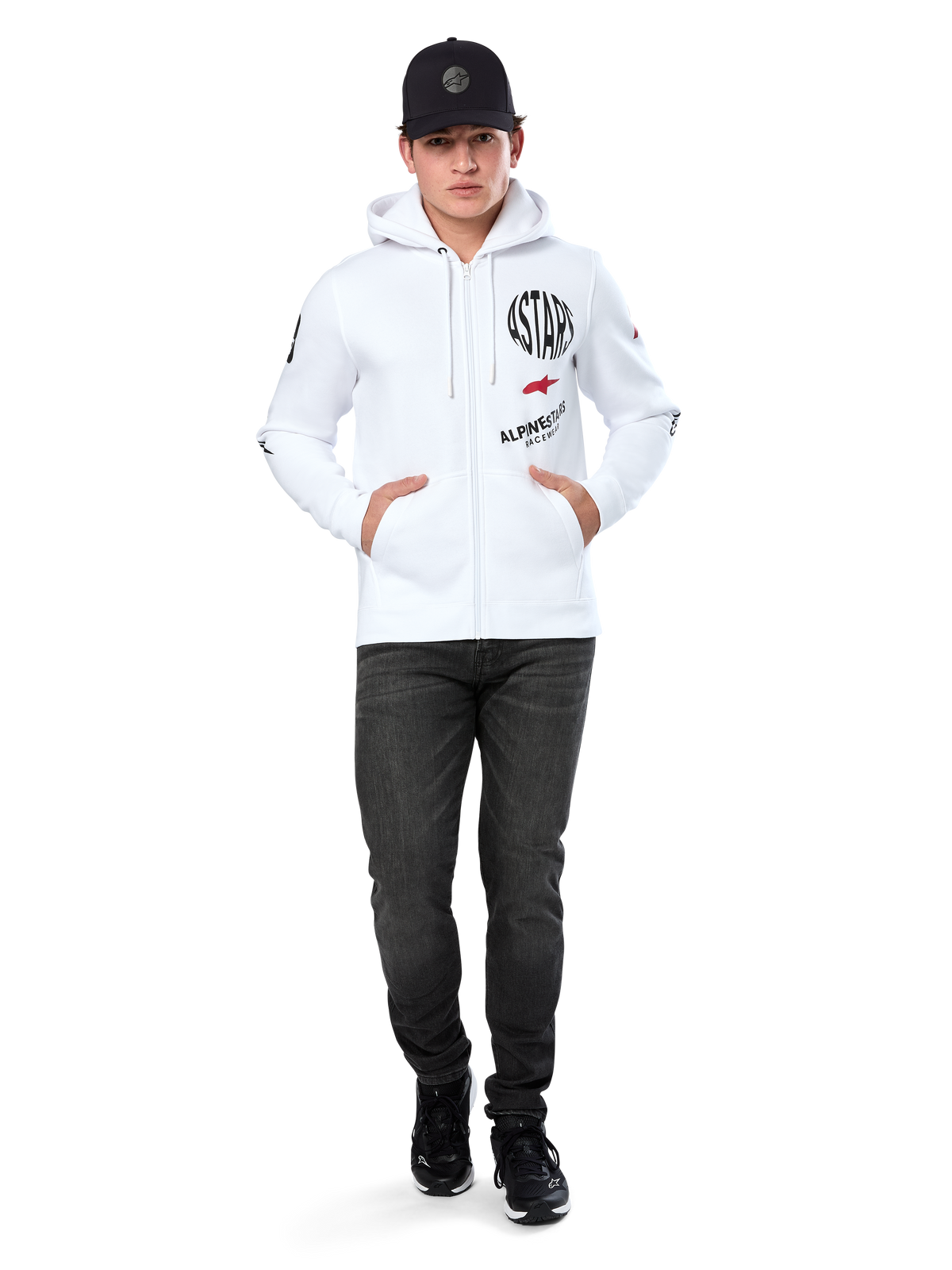 Felpa con cappuccio Alpinestars Variegate, felpa in pile bianca con zip, grafica multi-logo con scritta 'ASTARS' e logo a stella rosso sul petto, dettagli grafici sulle maniche, indossata da un modello con cappellino nero e jeans neri, abbigliamento streetwear casual motorsport
