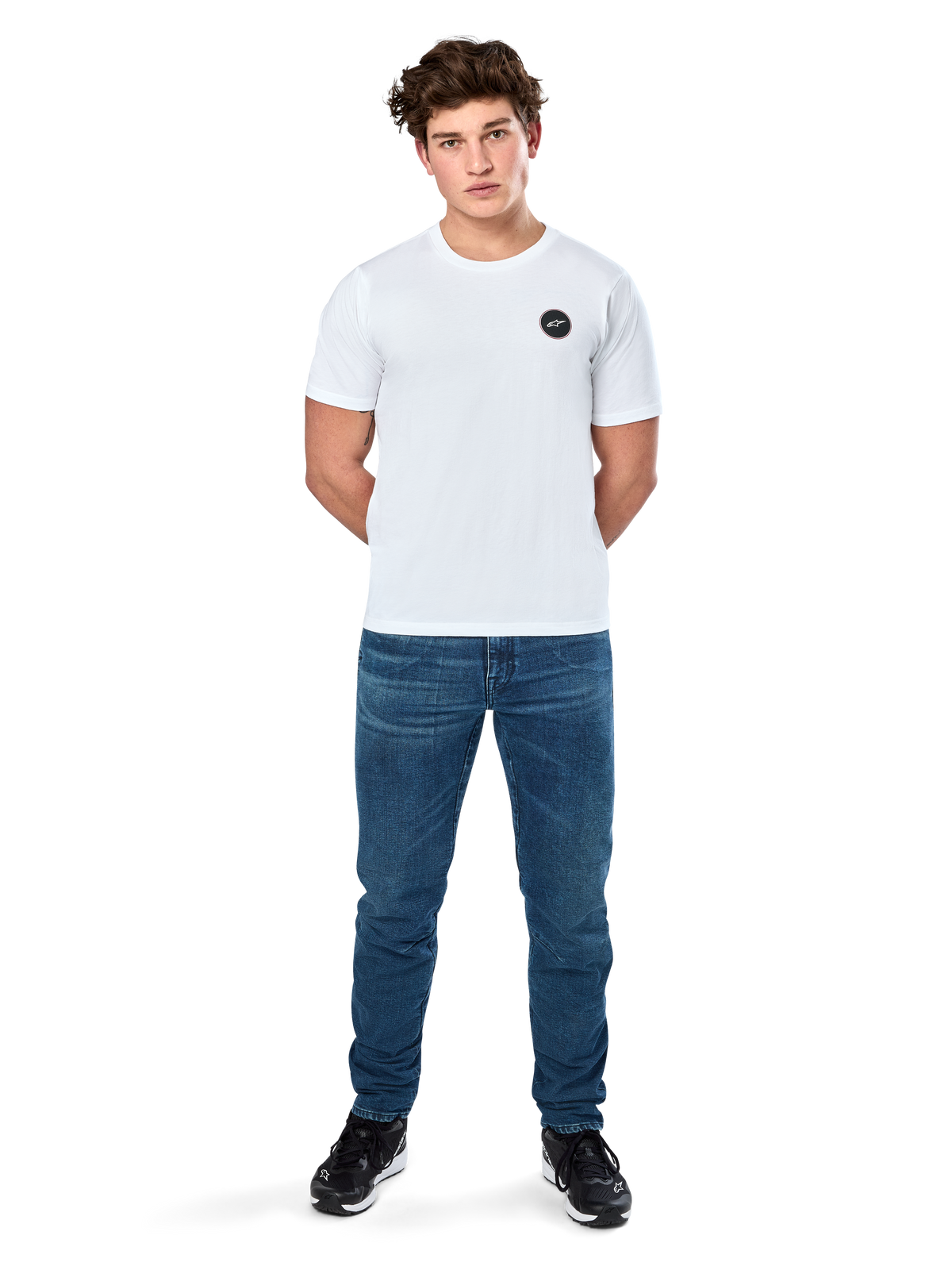 Alpinestars Dot Carbon Csf Tee, t-shirt a maniche corte, bianca, logo circolare Astars con effetto fibra di carbonio, abbigliamento casual motorsport, indossata da un modello con jeans blu e sneakers nere