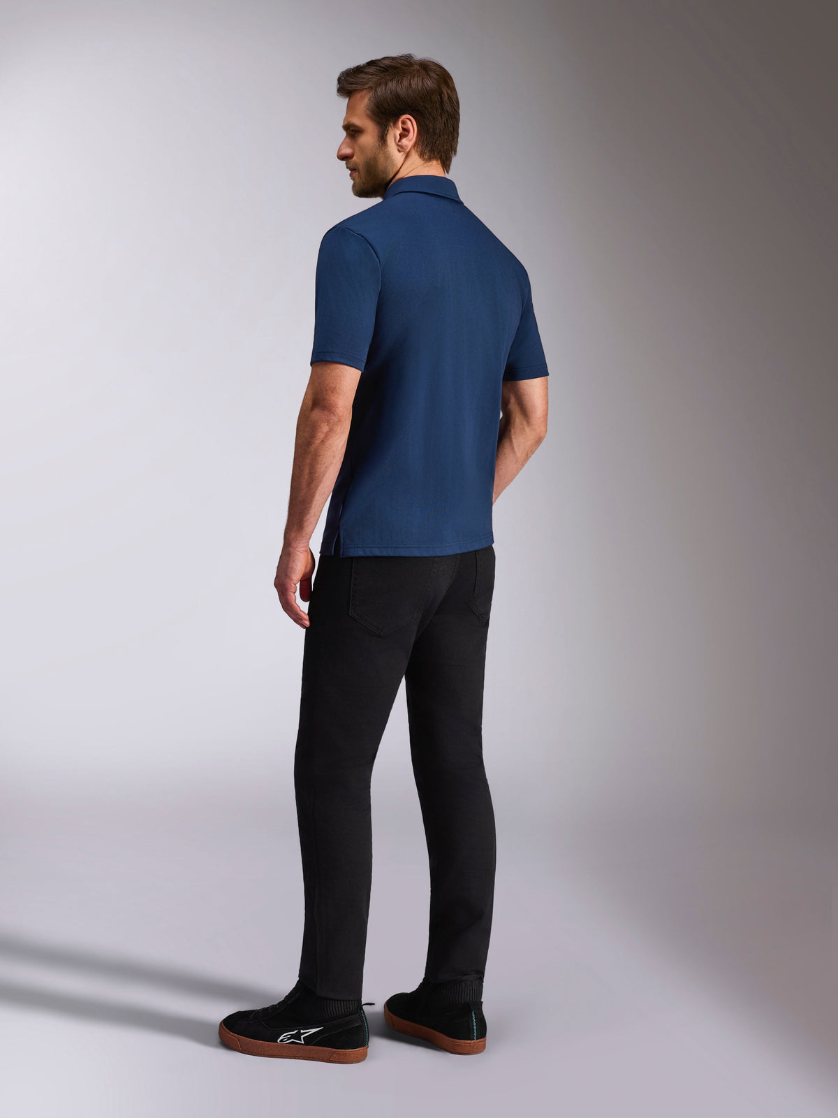 Polo Alpinestars Impetus Sport, polo a maniche corte blu navy, vista posteriore e laterale su modello, abbinata a pantaloni neri e sneakers nere, abbigliamento sportivo casual lifestyle motorsport