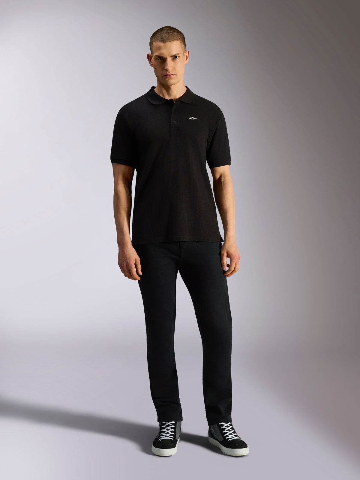 Alpinestars Polo Endeavor Classic, polo in piqué a maniche corte, nero, piccolo logo Astars bianco sul petto, colletto e polsini a coste, indossata da un modello con pantaloni neri e sneakers, abbigliamento streetwear casual motorsport