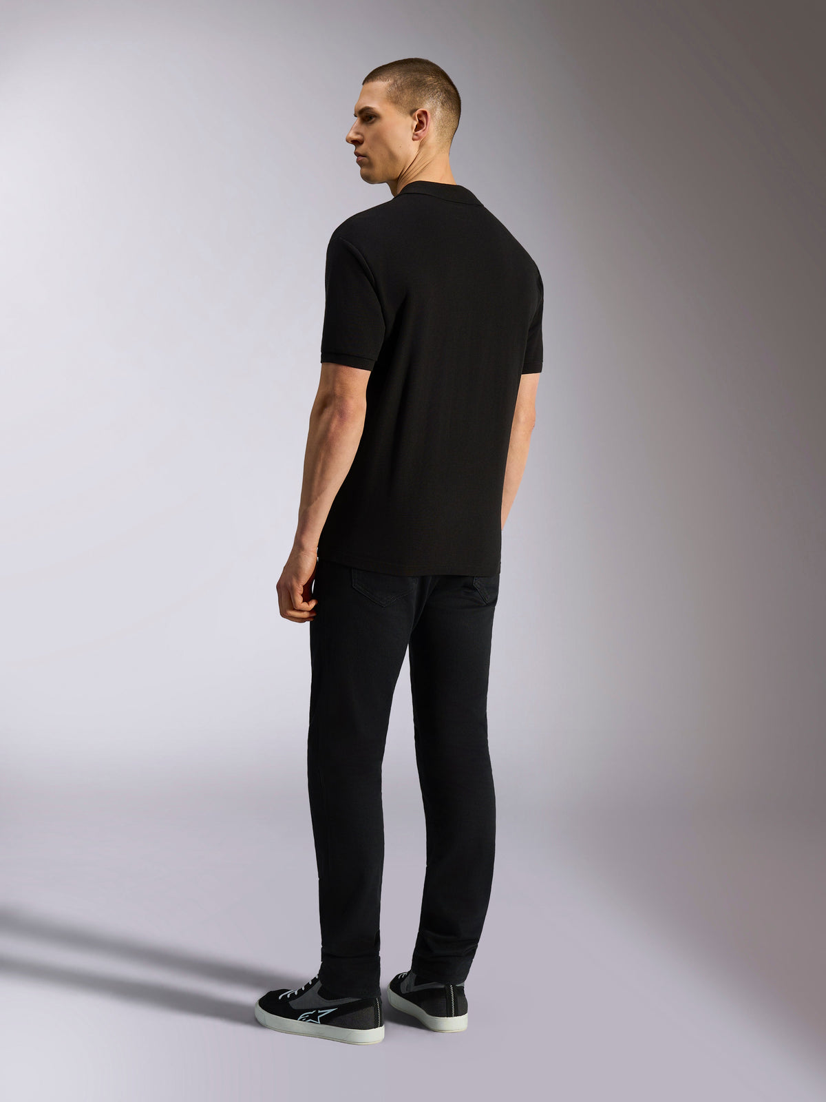 Polo Alpinestars Endeavor Classic, polo in piqué a maniche corte, nero, vista posteriore di un modello maschile con pantaloni neri e sneakers, streetwear casual ispirato al motorsport