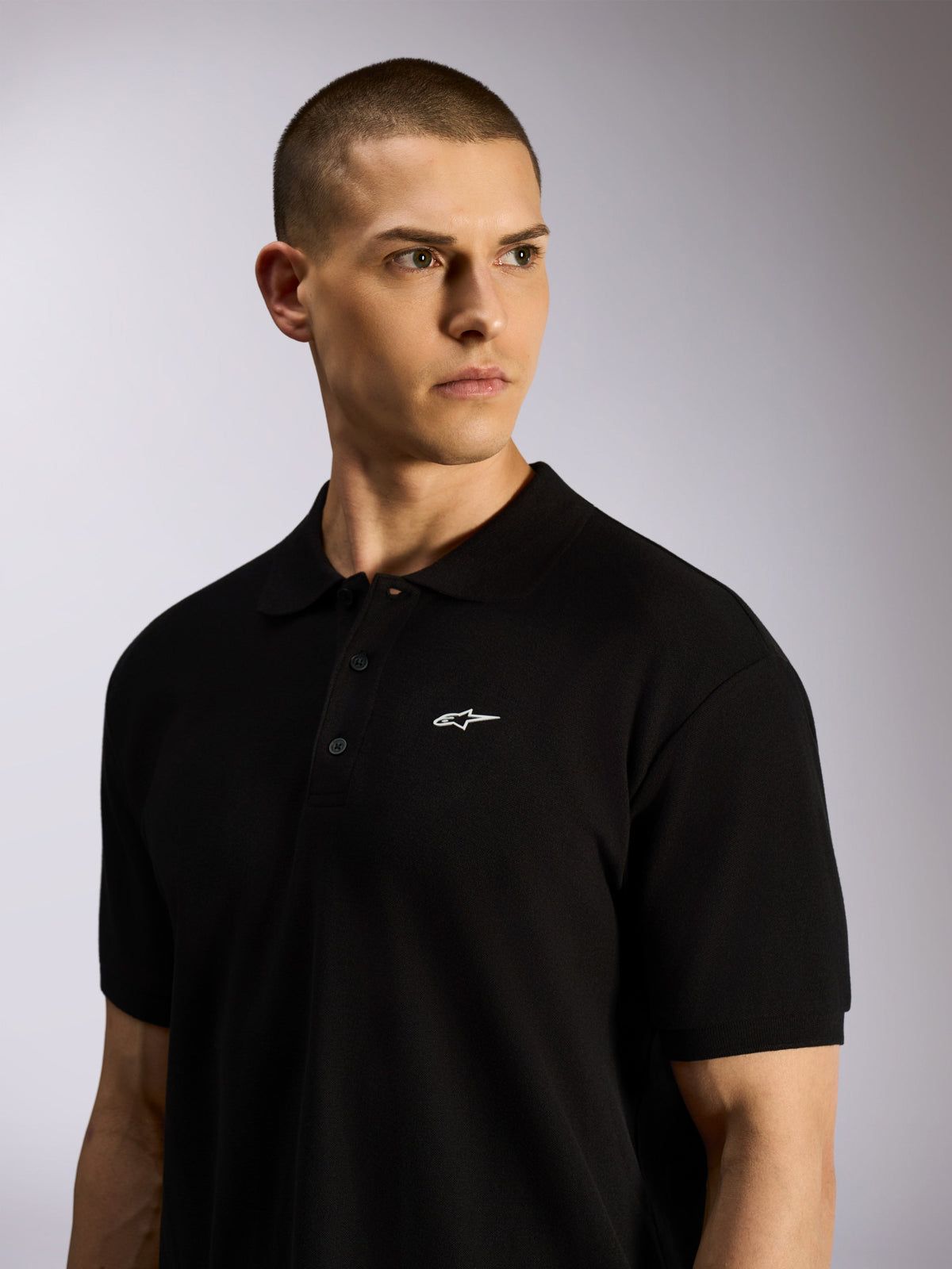 Alpinestars Polo Endeavor Classic, polo in piqué nera indossata da un modello, piccolo logo Astars bianco sul petto, chiusura a tre bottoni e colletto a coste, streetwear motorsport casual