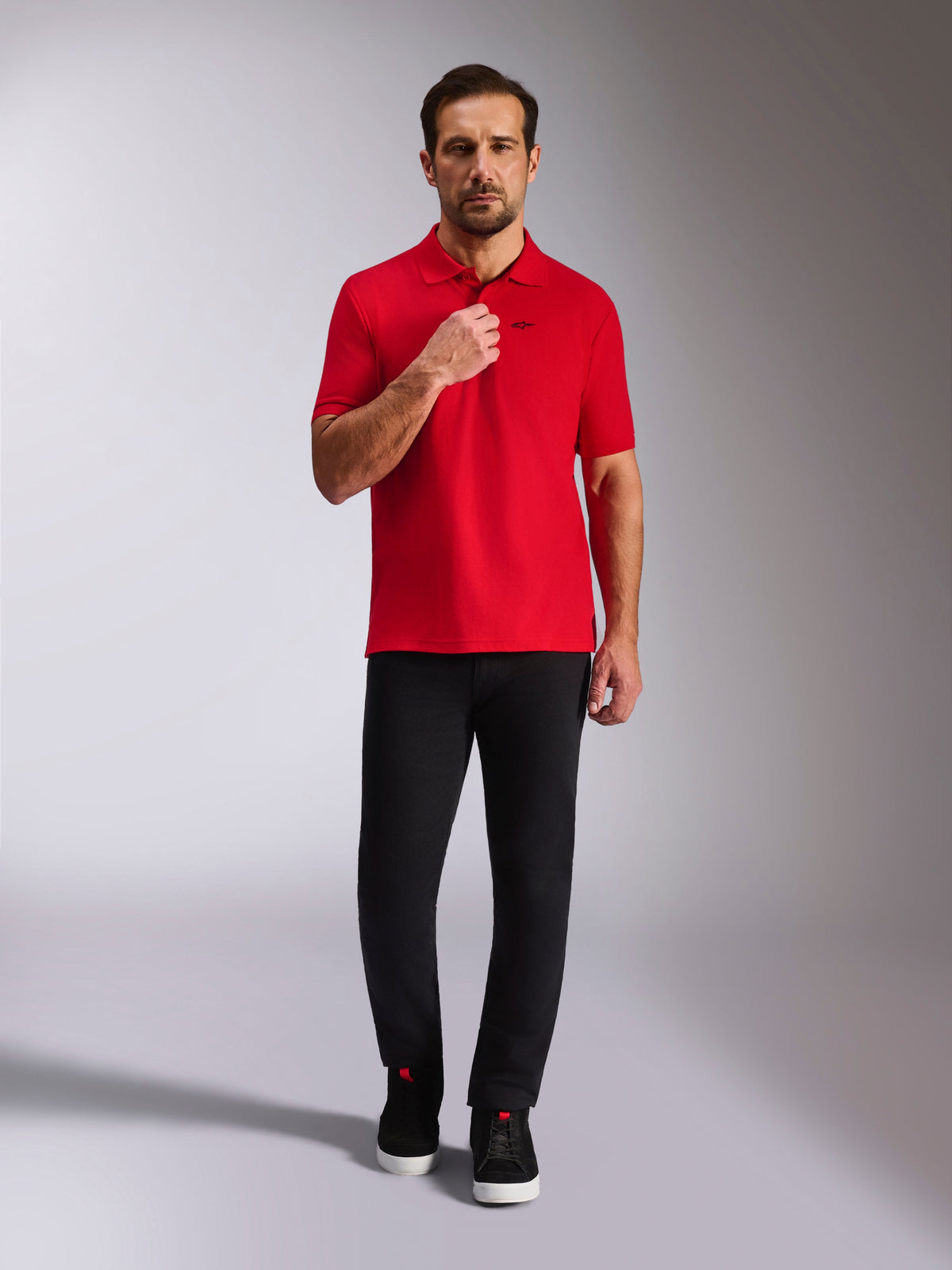 Polo Alpinestars Endeavor Classic, polo in piqué rossa, a maniche corte con logo Astars nero, colletto e polsini a coste, indossata con pantaloni neri e sneakers, streetwear casual d'ispirazione motorsport