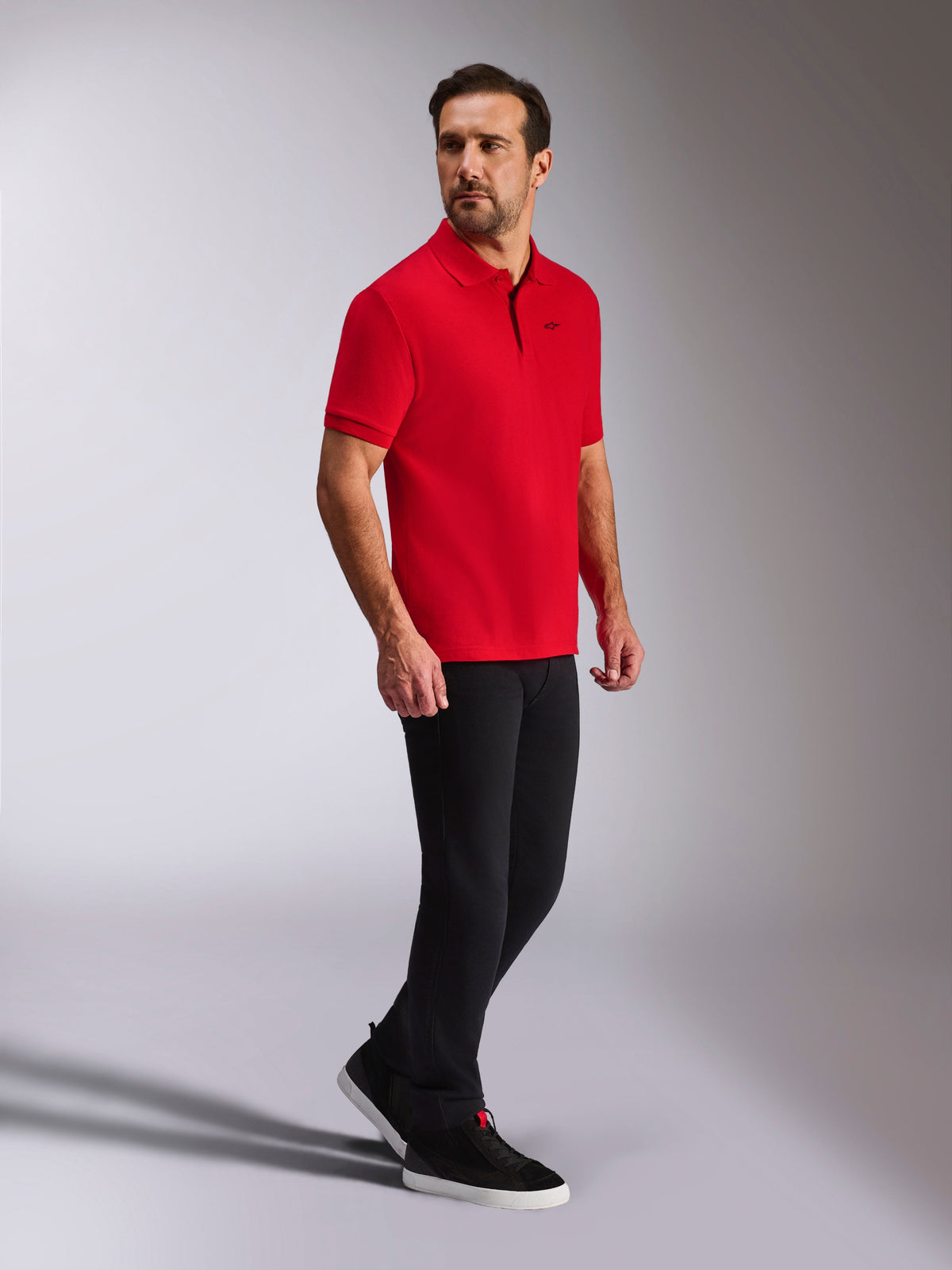 Alpinestars Endeavor Classic Polo, polo in piqué a maniche corte rossa, piccolo logo Astars nero, colletto e polsini a coste, indossata da un modello con pantaloni neri e sneakers, streetwear casual ispirato al motorsport