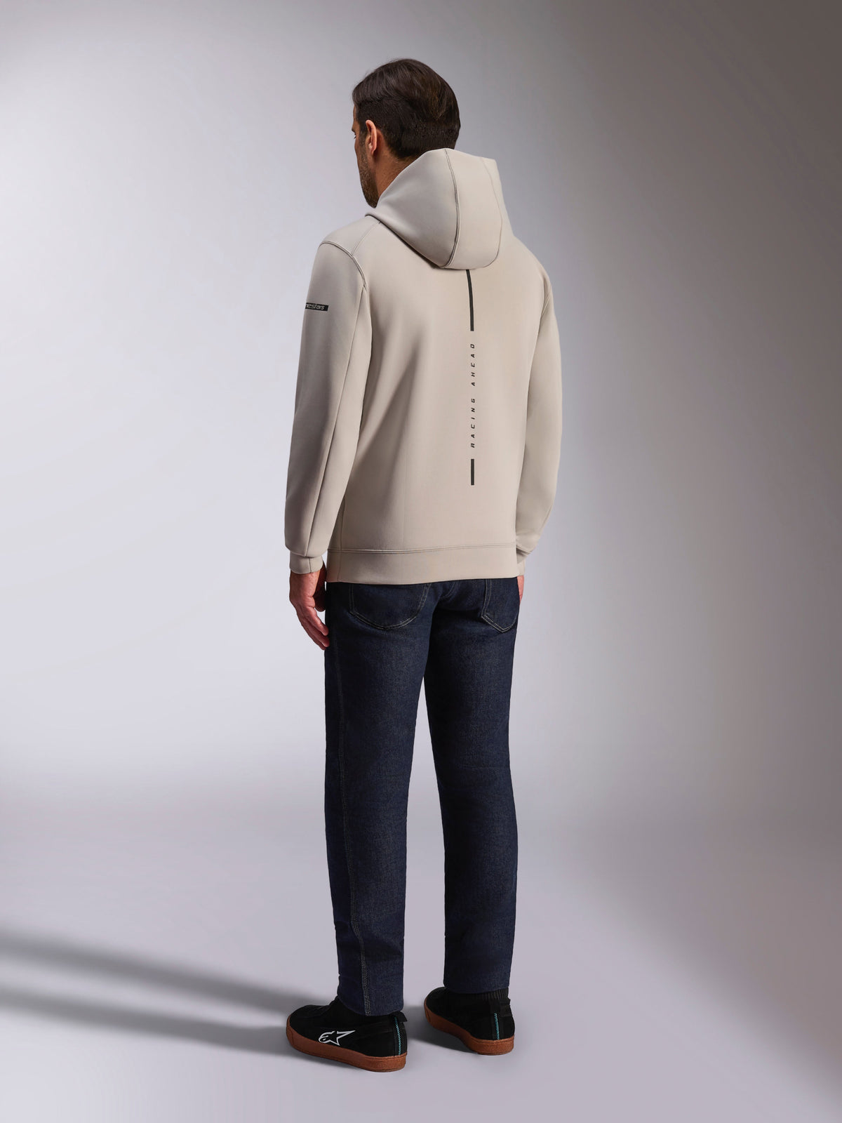 Felpa Alpinestars Insight, vista posteriore in grigio cemento, caratterizzata da una striscia nera verticale con la scritta 'RACING AHEAD', design casual streetwear, indossata con jeans scuri e scarpe nere.