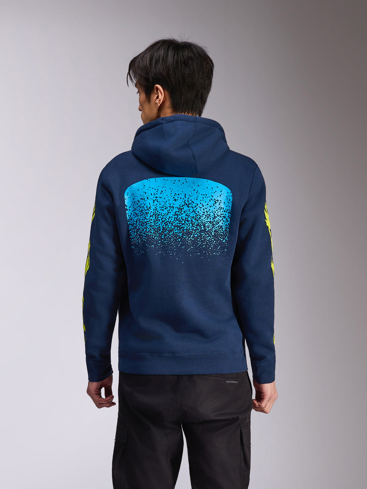 Alpinestars Obsessed Hoodie, felpa con cappuccio blu navy, vista posteriore con grande grafica a gradazione MX azzurra, marchio Alpinestars giallo sulle maniche, streetwear casual ispirato al motorsport