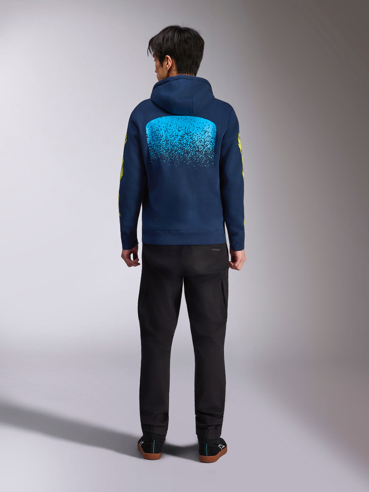 Alpinestars Obsessed Hoodie in blu navy, vista posteriore con grande grafica MX sfumata ciano e loghi gialli sulle maniche, felpa pullover casual ispirata al motorsport