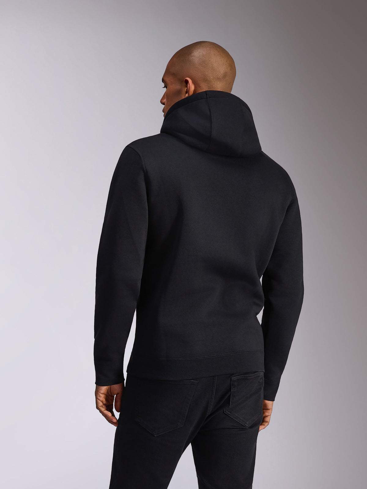 Alpinestars Ellipsoid Hoodie, nero, vista posteriore di una persona che indossa una felpa pullover con cappuccio, maniche lunghe con polsini e orlo a coste, abbinata a jeans neri, abbigliamento sportivo casual ispirato al motorsport