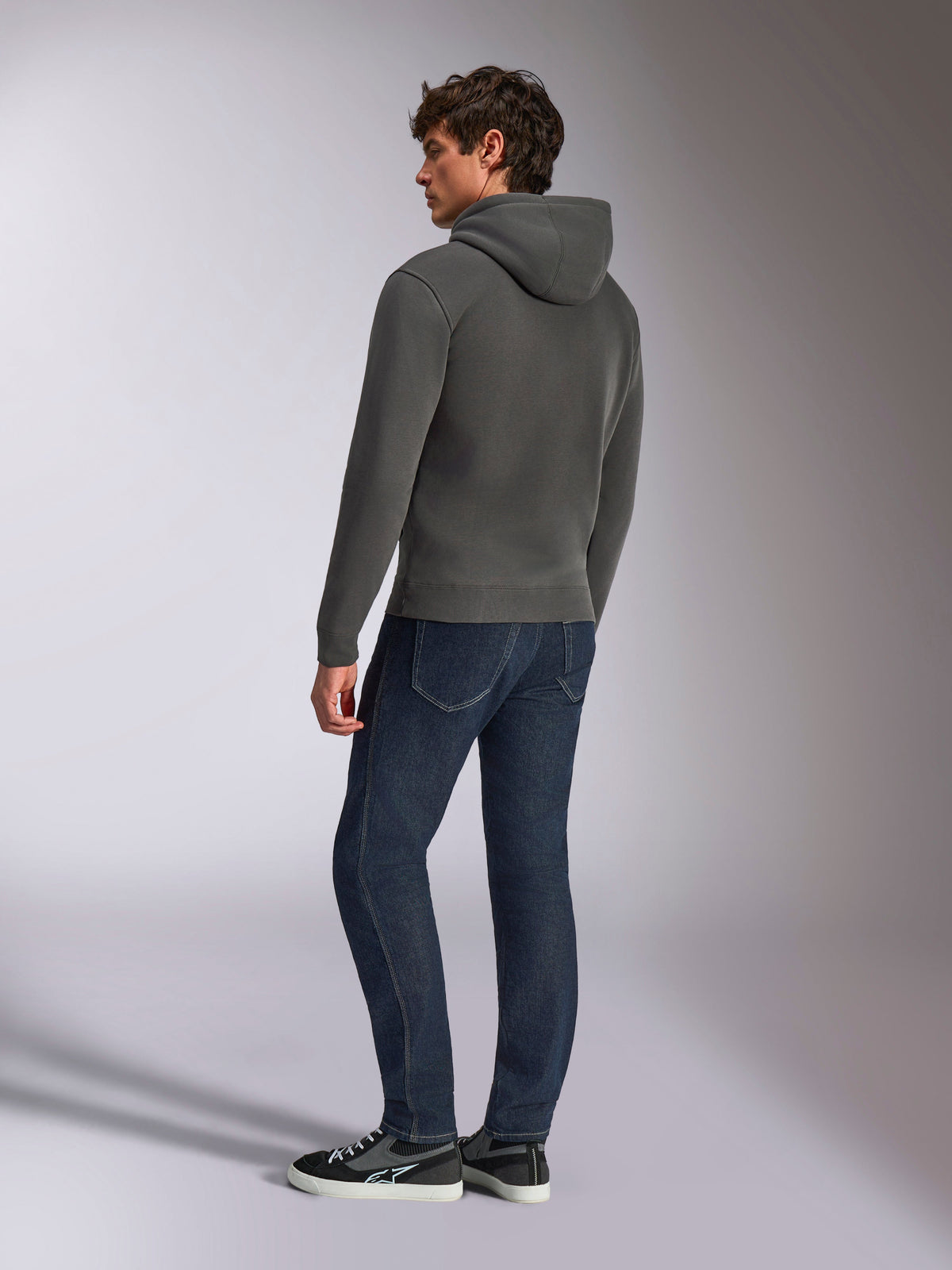 Felpa con cappuccio Alpinestars Ellipsoid, abbigliamento sportivo casual, grigio canna di fucile, vista posteriore su modello maschile, cappuccio con cordino, maniche lunghe, polsini e bordo a coste, abbinata a jeans scuri e sneakers