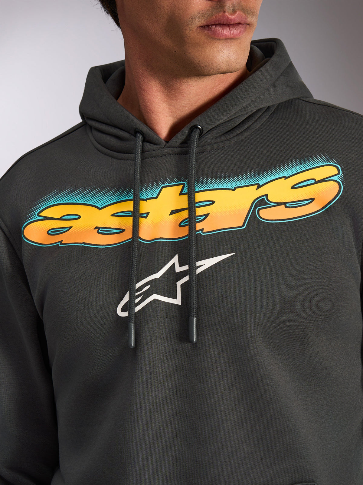 Alpinestars Ellipsoid Hoodie, Grigio Gunmetal, primo piano del petto con scritta 'astars' curva con gradiente da giallo ad arancione e accenti color ottanio, logo Alpinestars a stella bianco, felpa casual streetwear ispirata al motorsport