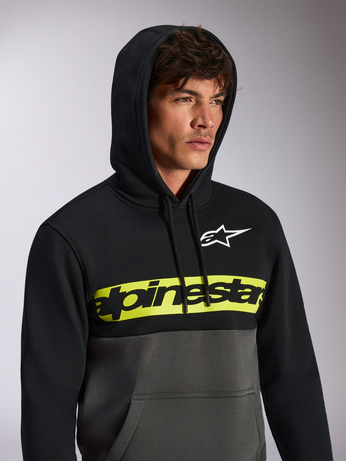 Felpa con cappuccio Alpinestars Parallel, streetwear casual a blocchi di colore, parte superiore nera e parte inferiore grigio gunmetal, fascia gialla neon sul petto con logo Alpinestars nero, logo Astars bianco, felpa pullover con cappuccio e coulisse