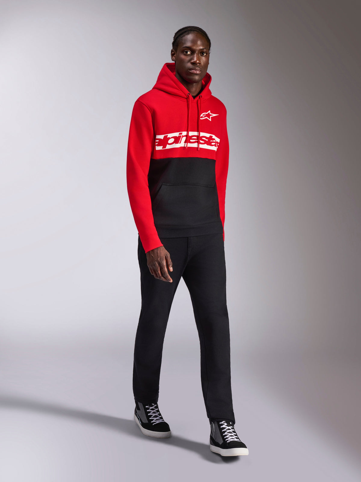 Alpinestars Parallel Hoodie, sportswear casual, design a blocchi di colore rosso e nero, con marchio Alpinestars bianco e logo a stella sul petto, indossata con pantaloni neri e sneakers, look moderno ispirato al motorsport
