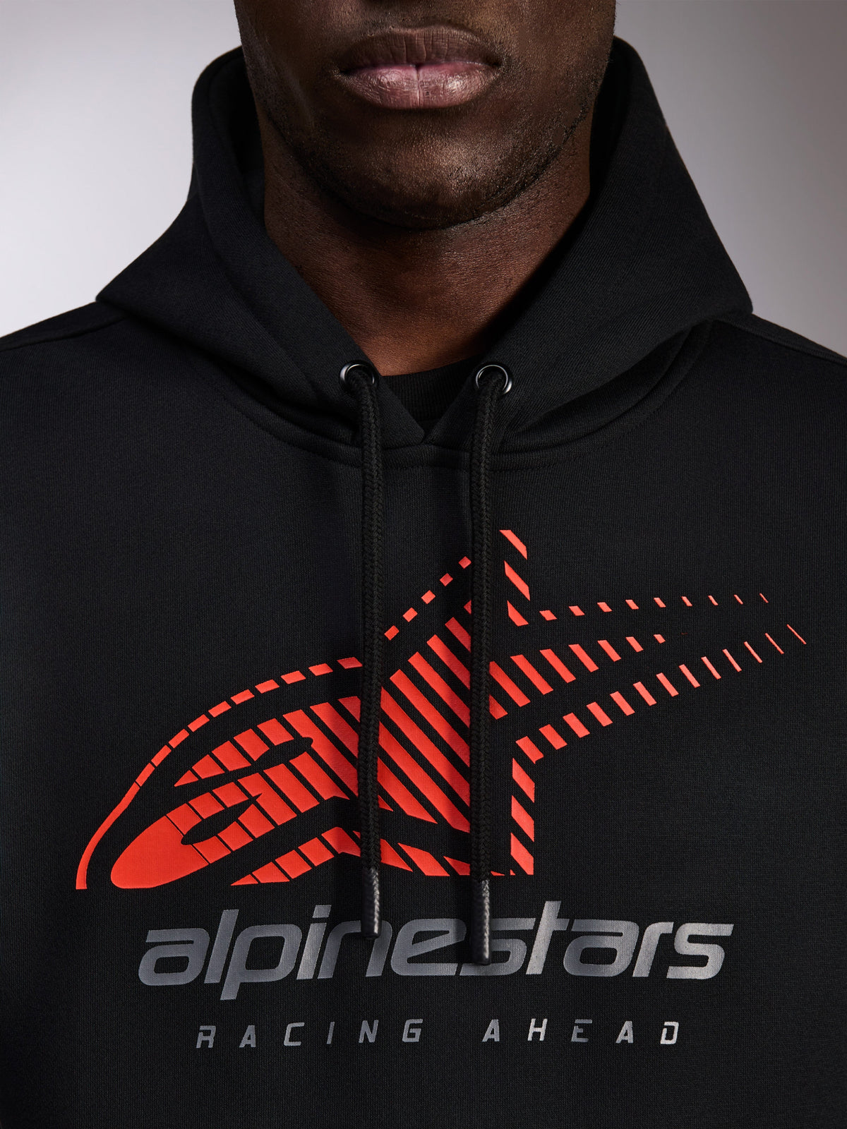 Alpinestars Pulse Hoodie, felpa nera con cappuccio, primo piano del petto con logo Astars rosso con linee di velocità sfumate e marchio argento, cordini neri con estremità immerse, streetwear casual motorsport
