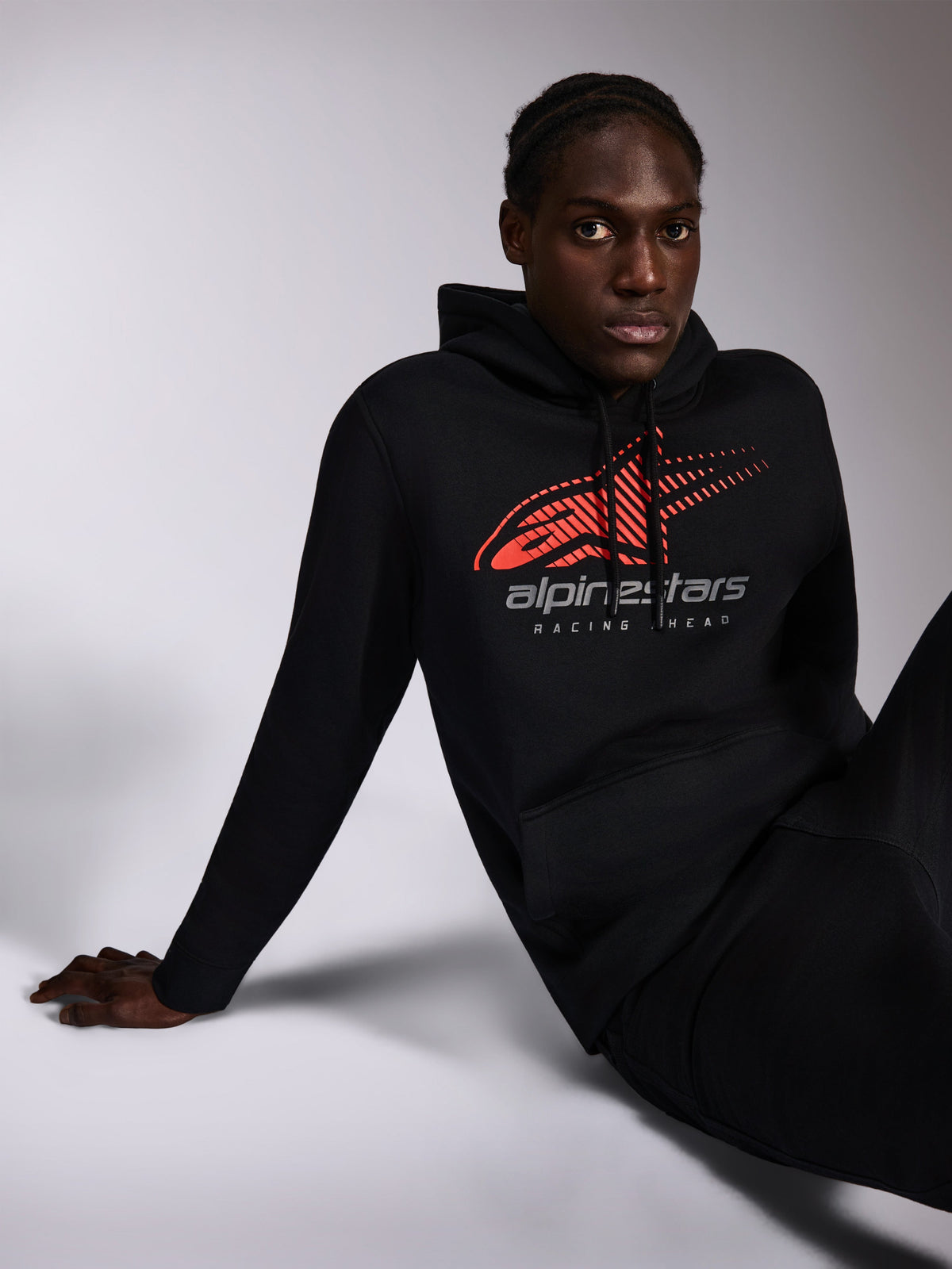 Felpa con cappuccio Alpinestars Pulse, nero, streetwear casual indossato da un modello, con logo Astars rosso con linee di velocità sfumate e scritta 'alpinestars RACING AHEAD' sul petto, cappuccio con cordino, maniche lunghe, design moderno ispirato al motorsport