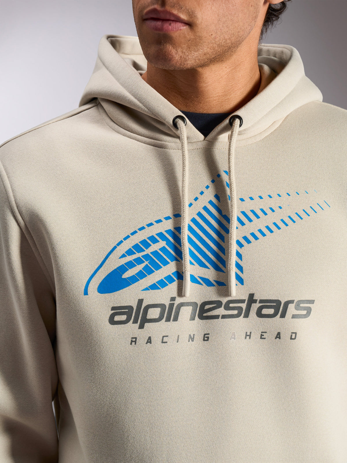 Felpa con cappuccio Alpinestars Pulse, pullover casual streetwear Off White, primo piano del petto con logo Astars Combo blu e grigio con sfumatura a linee di velocità e scritta 'Racing Ahead', cappuccio con cordino ed estremità immerse.