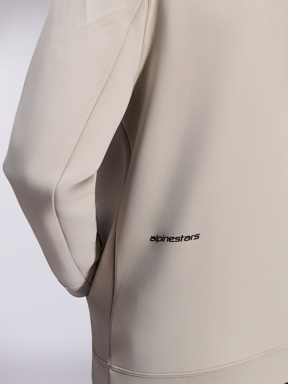 Alpinestars Cypher Hoodie, felpa con zip in pile double face, grigio Cement, primo piano del piccolo logo Alpinestars nero sulla parte bassa della schiena, dettaglio della tasca sulla cucitura e della trama liscia del tessuto