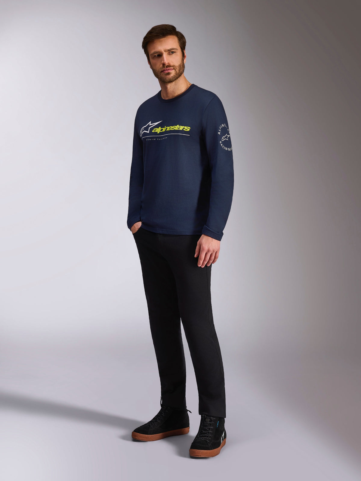 Alpinestars Mandatory CSF Tee, maglietta a maniche lunghe, navy, con logo Astars bianco e marchio Alpinestars giallo sul davanti, logo circolare Astars sulla manica, indossata da un modello con pantaloni neri e sneaker nere per un look lifestyle casual