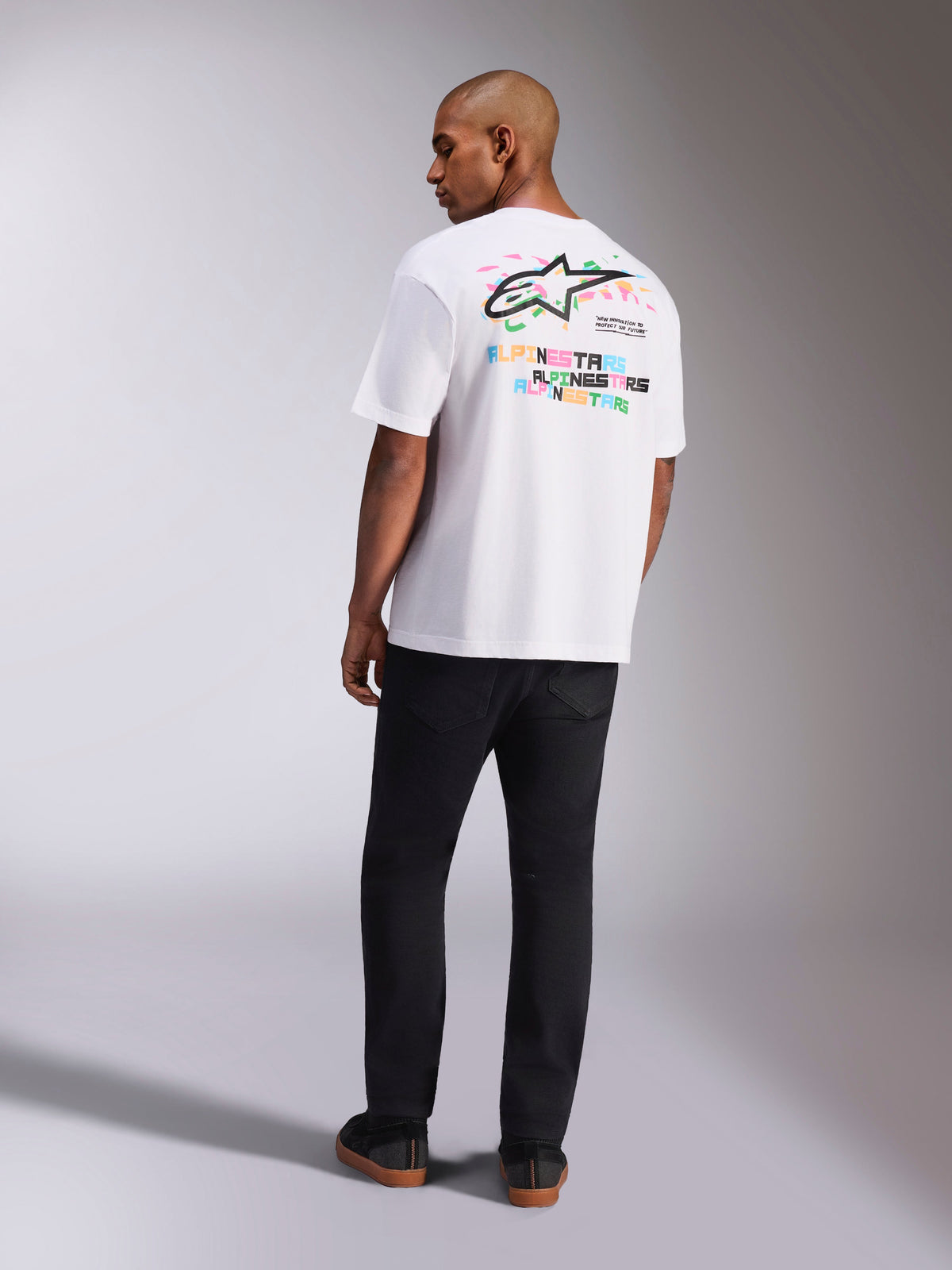 Alpinestars Wild Oversized CSF Tee, t-shirt a maniche corte, bianco, vista posteriore del modello che indossa la t-shirt oversize con vivace logo Astars multicolore e scritte sul retro, streetwear casual ispirato al motorsport