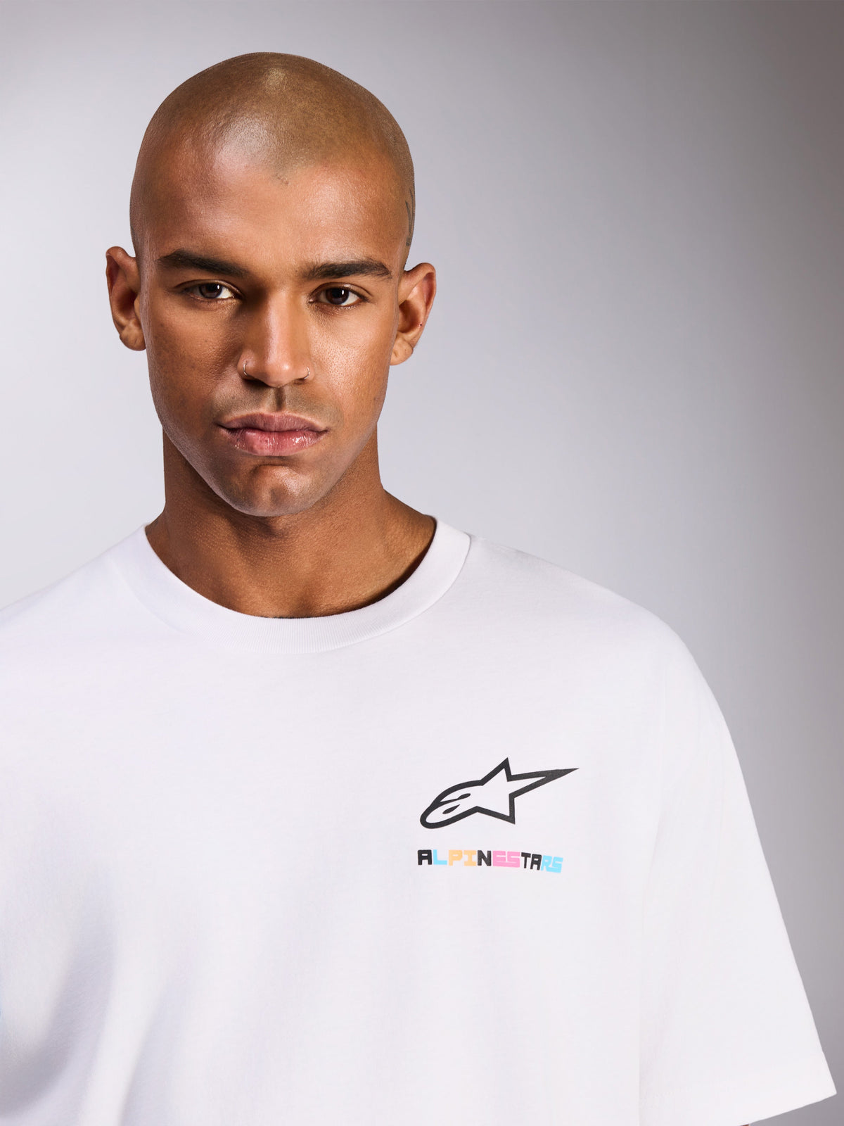 Modello che indossa la T-shirt Alpinestars Wild Oversized CSF, maglietta a maniche corte bianca, con logo Astars nero e scritte multicolore vivaci sul petto, stile casual streetwear