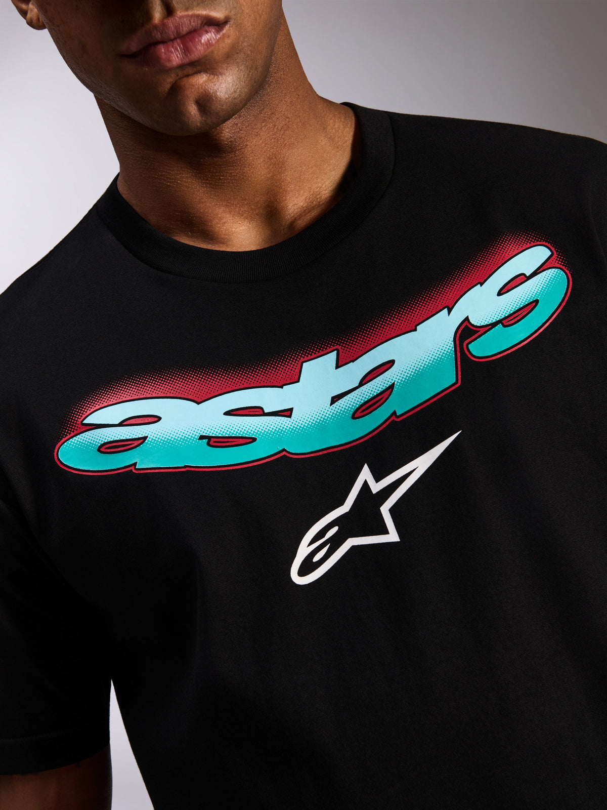 Alpinestars Ellipsoid CSF Tee, maglietta a maniche corte, nero, primo piano della grafica frontale con scritta Astars sfumata in verde acqua e blu, ombra rossa a effetto retinato e logo a stella bianco, abbigliamento casual motorsport streetwear