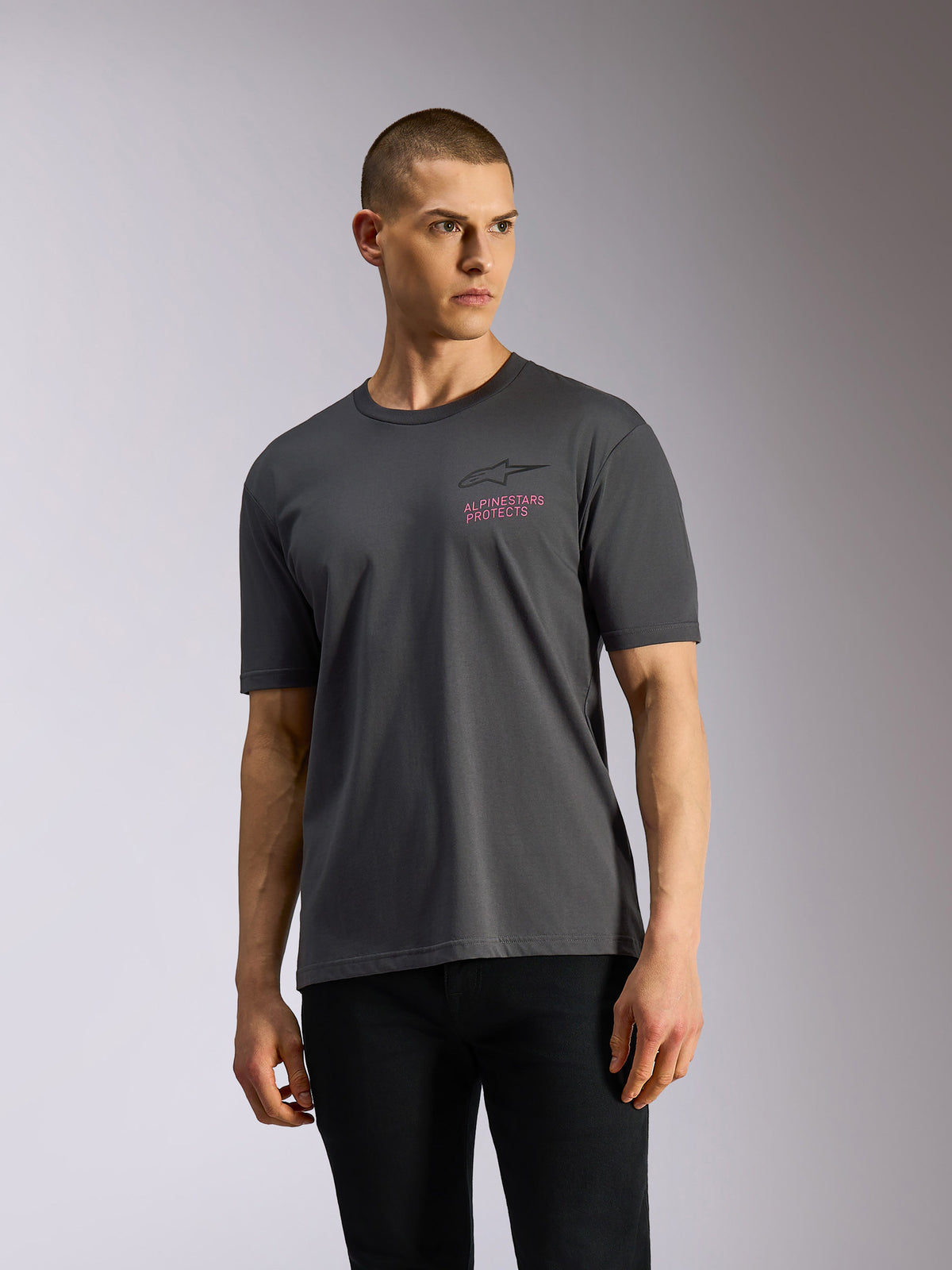 Alpinestars Pop Helmet CSF Tee, maglietta a maniche corte, grigio antracite, indossata da un modello, con logo Astars nero e scritta rosa 'ALPINESTARS PROTECTS' sul petto, streetwear casual motorsport