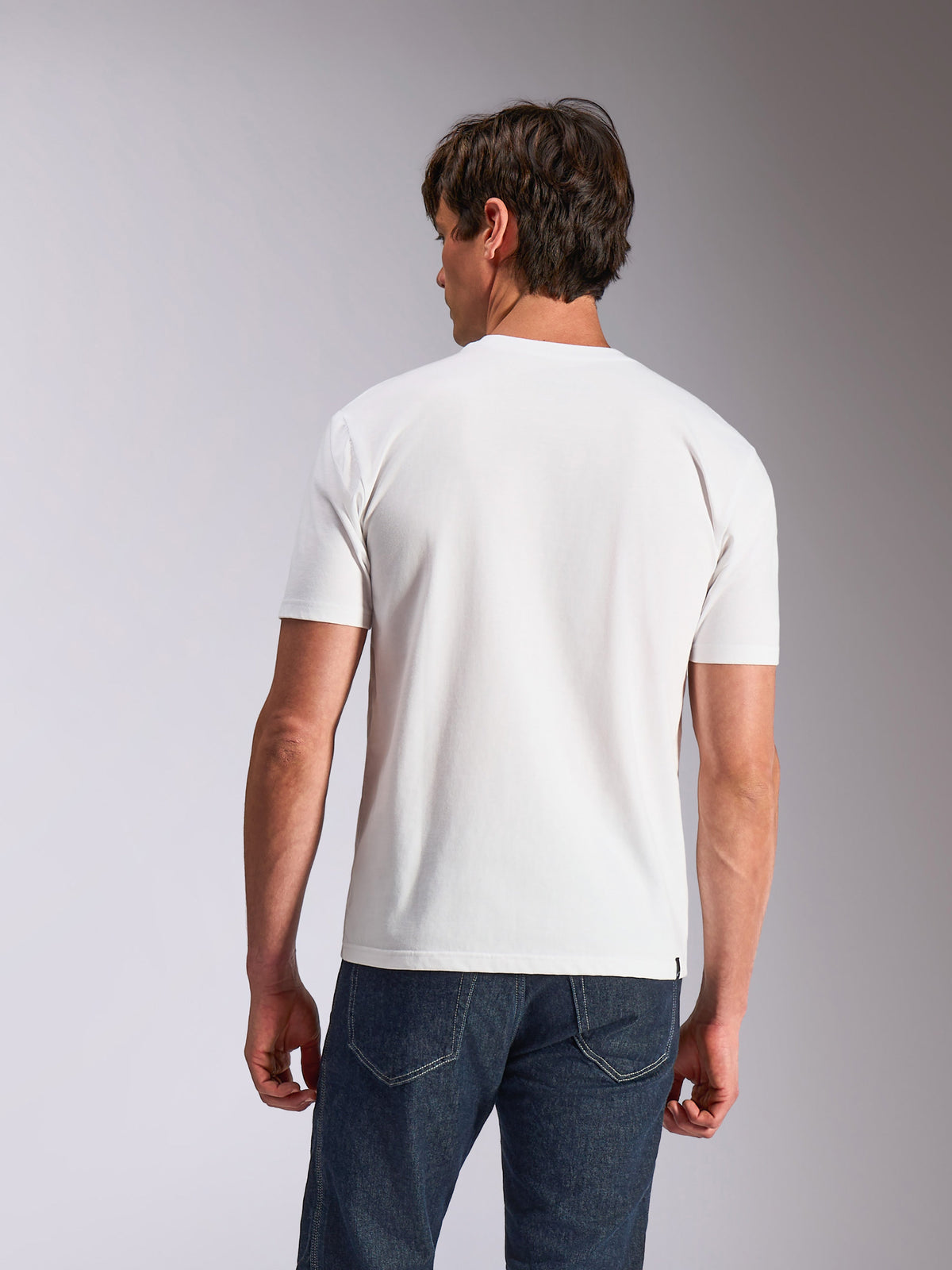 Alpinestars Abus CSF Tee, t-shirt a maniche corte, bianco, vista posteriore del modello che indossa una t-shirt bianca semplice e jeans blu scuro, abbigliamento lifestyle casual ispirato al motorsport