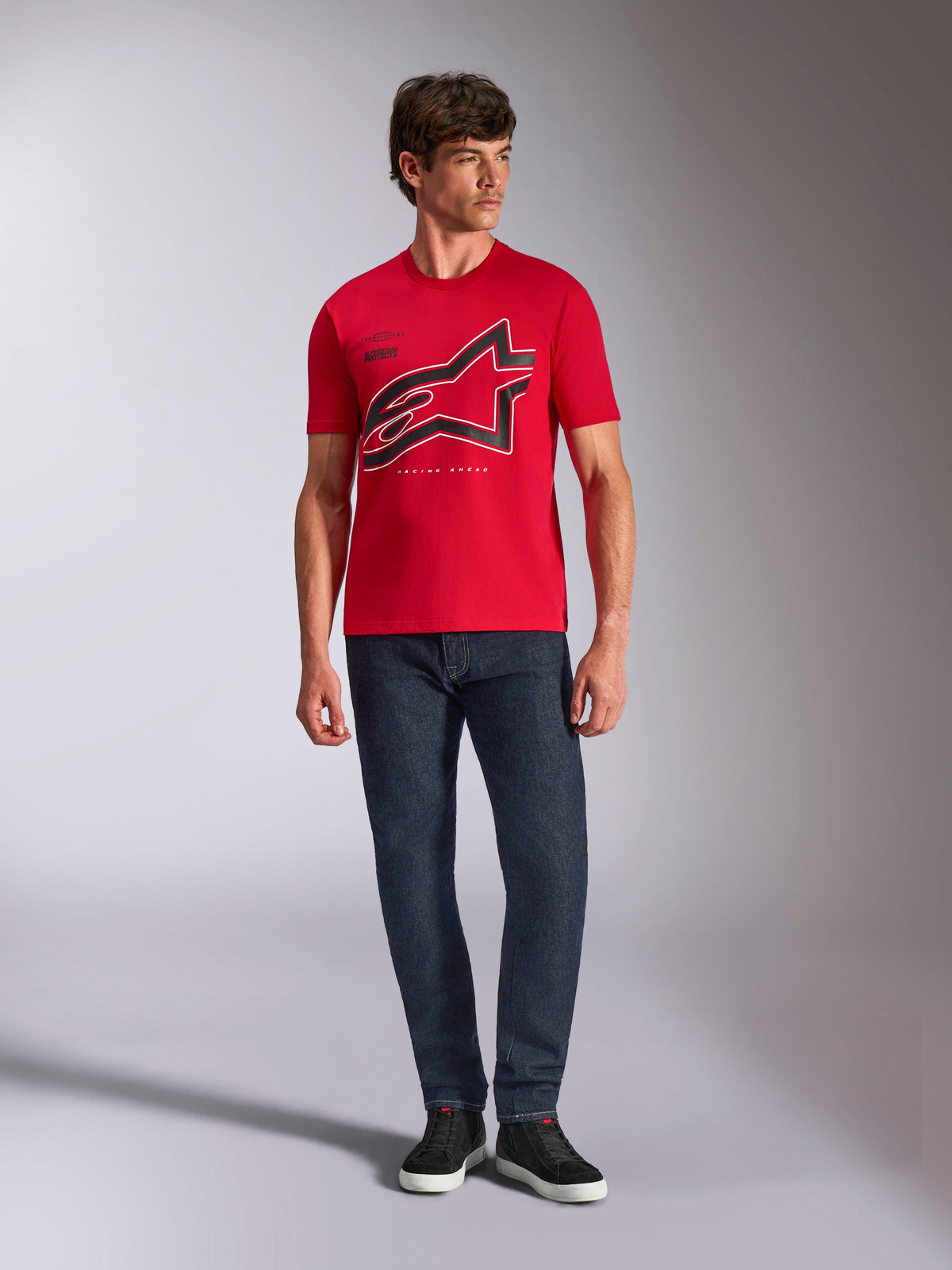 Alpinestars Authority CSF Tee, T-shirt a maniche corte, rossa, grande logo Astars nero ritagliato con contorno bianco, indossata con jeans blu scuro e sneakers nere, streetwear casual ispirato al motorsport