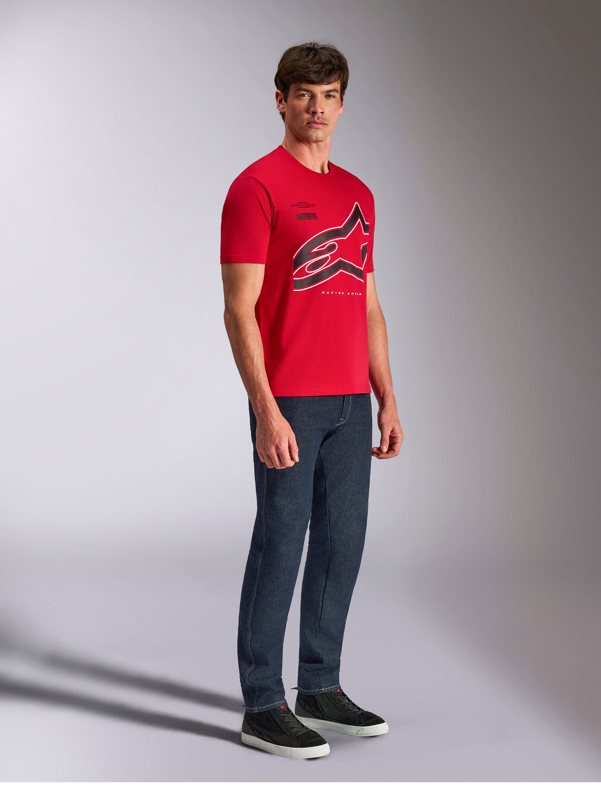 Alpinestars Authority CSF Tee, t-shirt a maniche corte, rosso, grande logo Astars ritagliato con contorni neri e bianchi, indossata da un modello con pantaloni in denim scuro e sneakers nere, streetwear casual ispirato al motorsport