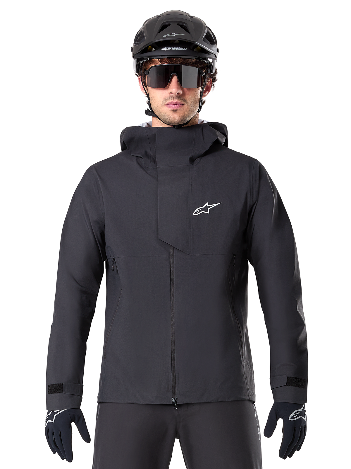Giacca Alpinestars A-Dura Elite Waterproof, nero, giacca da mountain bike, design a collo alto con cappuccio, cerniera frontale con patta protettiva sul petto e logo bianco, indossata con casco nero e guanti da ciclismo, protezione tecnica contro le intemperie per il trail riding