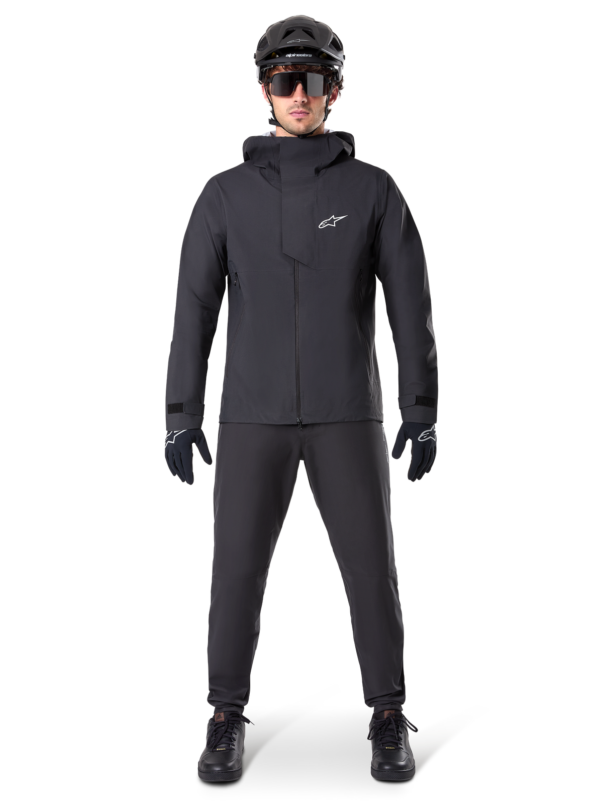 Giacca impermeabile Alpinestars A-Dura Elite, colore nero, indossata con pantaloni da ciclismo e guanti coordinati, casco e occhiali da sole neri, con logo Astars bianco sul petto, design tecnico ad alte prestazioni per mountain bike