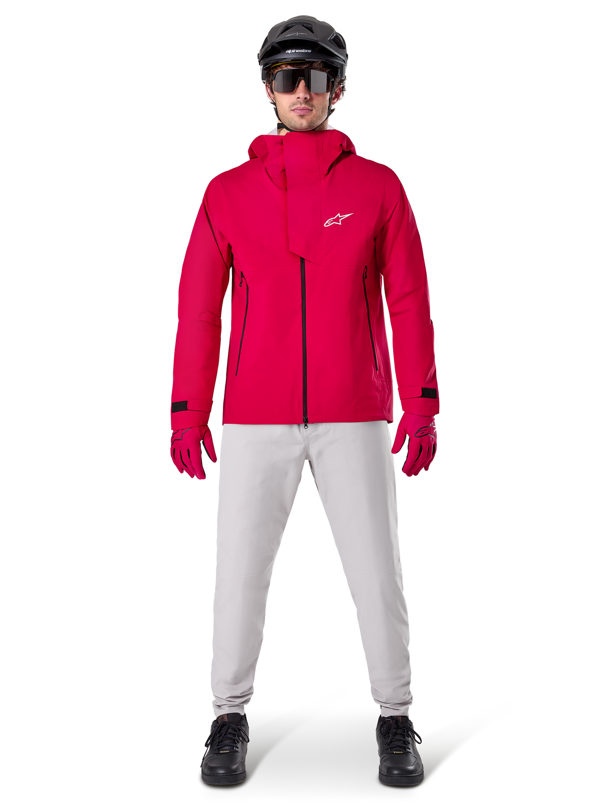 Giacca impermeabile Alpinestars A-Dura Elite, Rosso Fluo, giacca tecnica da mountain bike indossata con un casco da MTB nero, occhiali da sole, guanti rossi coordinati e pantaloni grigio chiaro, vista a figura intera dell'abbigliamento da ciclismo per tutte le condizioni atmosferiche