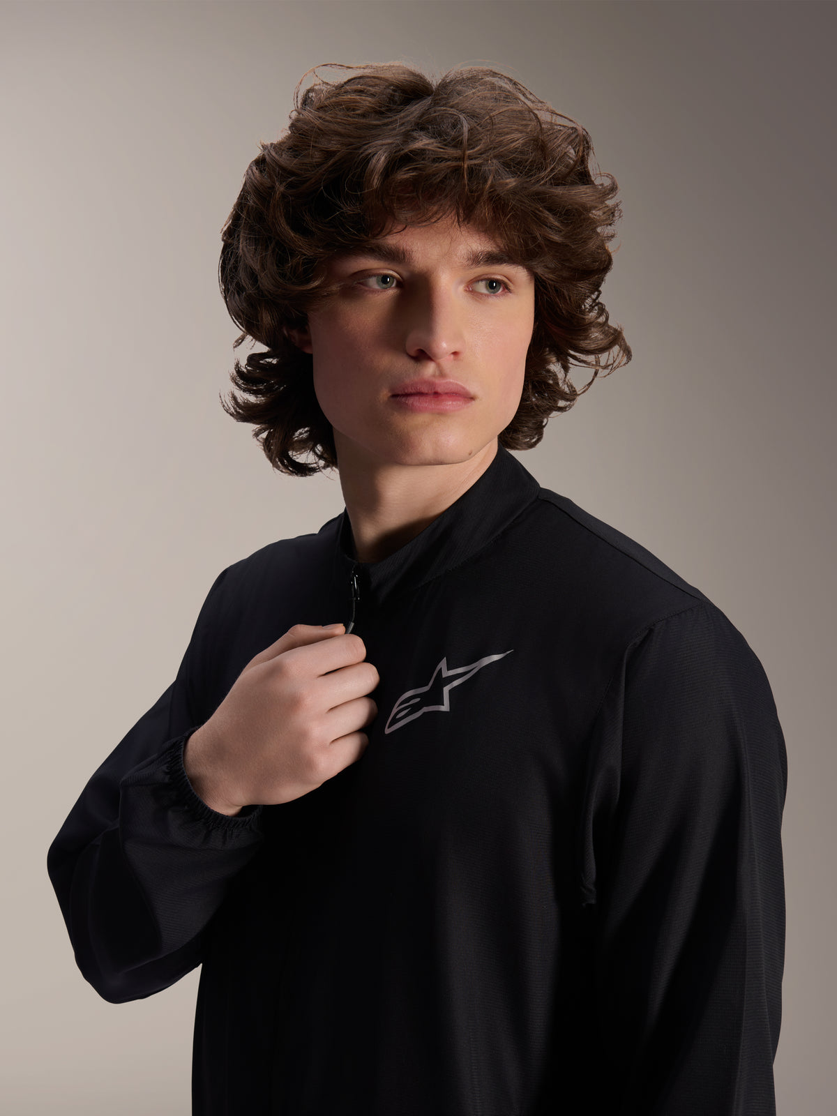Giacca frangivento Alpinestars A-Aria, giacca da ciclismo nera, indossata da un modello uomo, design con collo alto e logo Astars argento sul petto, attrezzatura MTB performante leggera e resistente al vento