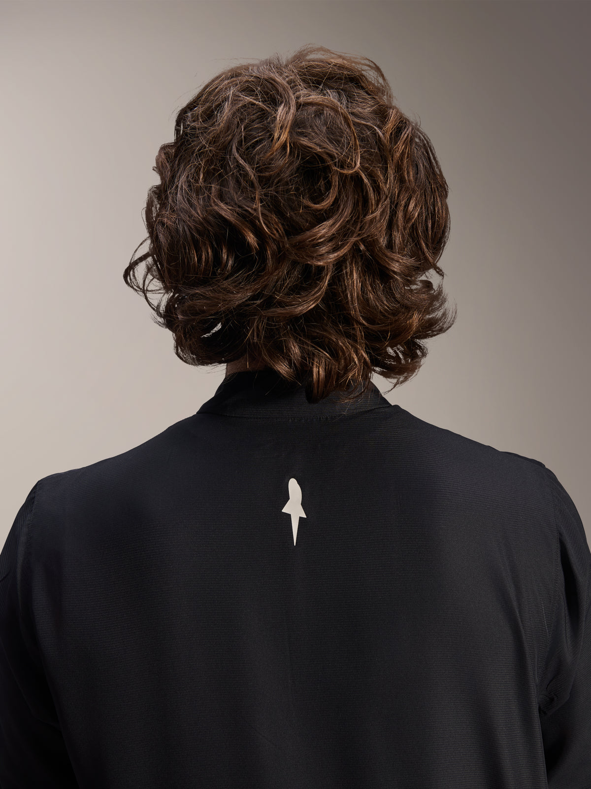 Giacca Frangivento Alpinestars A-Aria, nero, vista posteriore ravvicinata della parte superiore delle spalle e del colletto, con un piccolo logo bianco al centro della schiena, indossata da un modello con capelli castani mossi, abbigliamento tecnico da ciclismo minimalista