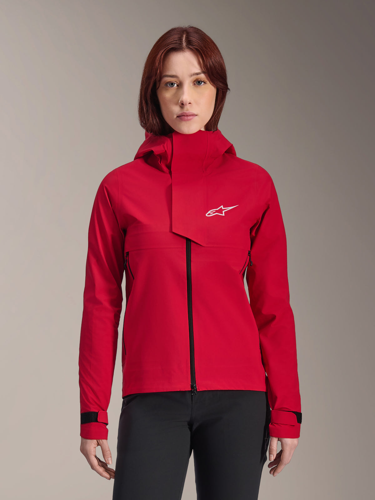 Alpinestars Stella A-Dura Elite Waterproof Jacket, giacca da mountain bike da donna, rosso fluo, design con cappuccio e patta frontale asimmetrica, logo Alpinestars bianco sul petto, polsini neri regolabili, indossata da una modella con pantaloni neri
