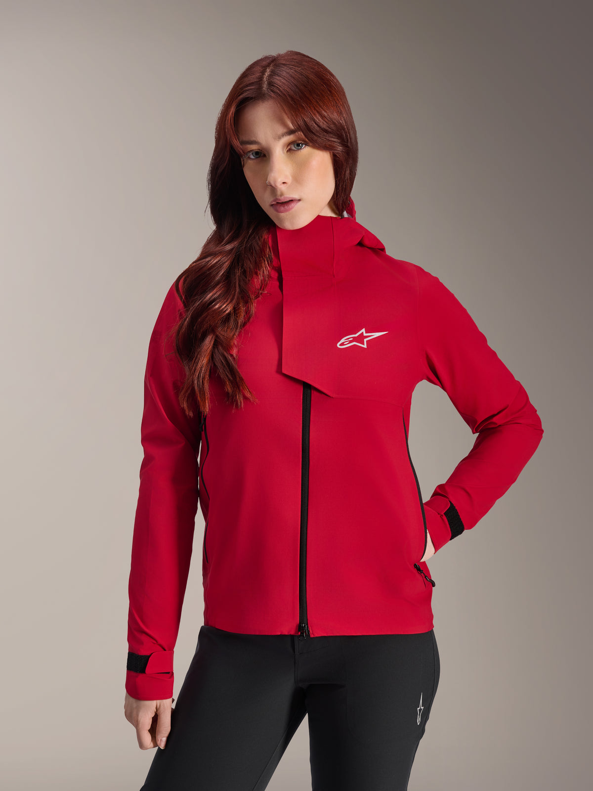 Giacca impermeabile Alpinestars Stella A-Dura Elite, giacca da mountain bike da donna, Rosso Fluo, con patta antivento anteriore dotata di logo Alpinestars bianco, collo alto e polsini regolabili, indossata con pantaloni neri per un look tecnico da riding