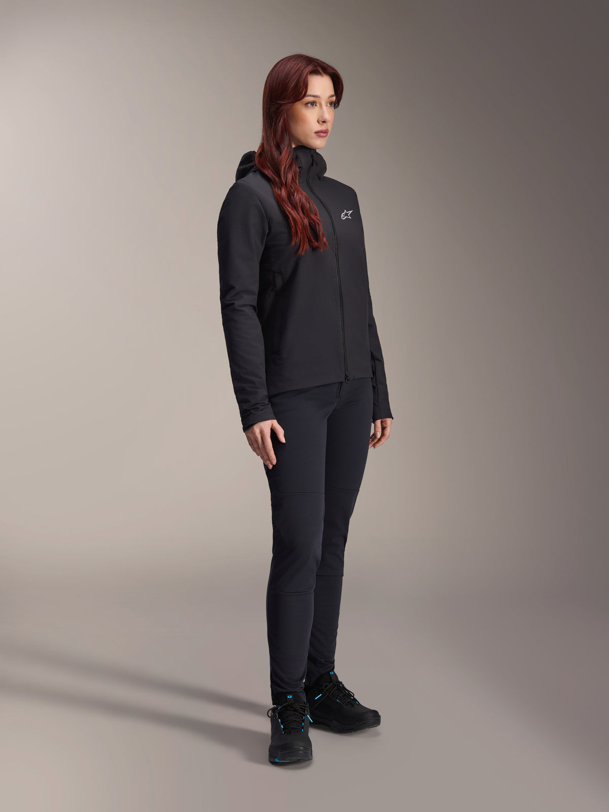 Alpinestars Giacca Termica Stella A-Dura, giacca isolante leggera da donna con cappuccio in nero, indossata con pantaloni neri e scarpe nere, completo professionale da ciclismo e mountain bike per il freddo