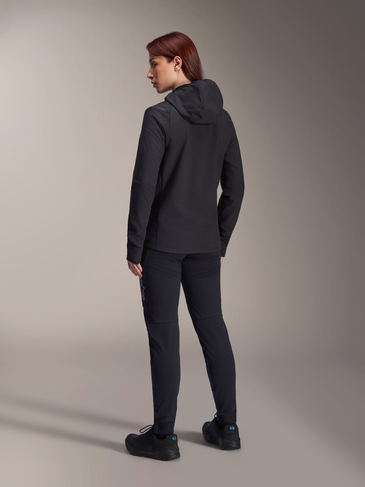 Giacca Termica Stella A-Dura Alpinestars, giacca da ciclismo MTB da donna, nero, vista posteriore che mette in risalto il cappuccio isolato e la vestibilità regolare, indossata con pantaloni e scarpe neri coordinati, isolamento termico leggero per la guida in climi freddi